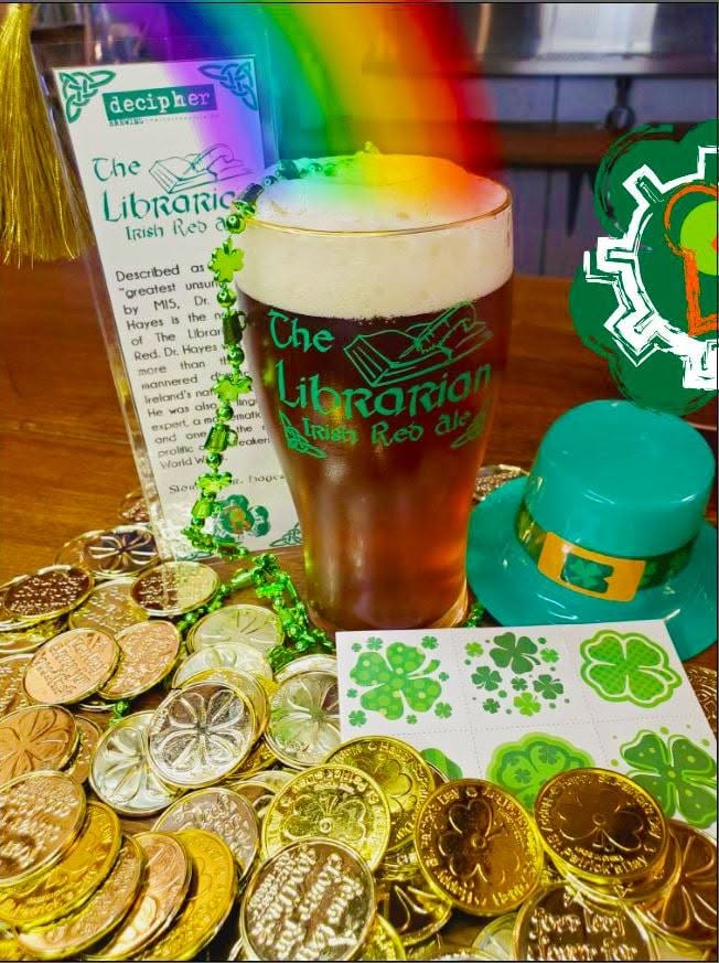A glass of beer with foam, surrounded by gold coins, green shamrocks, and St. Patrick's Day decorations.