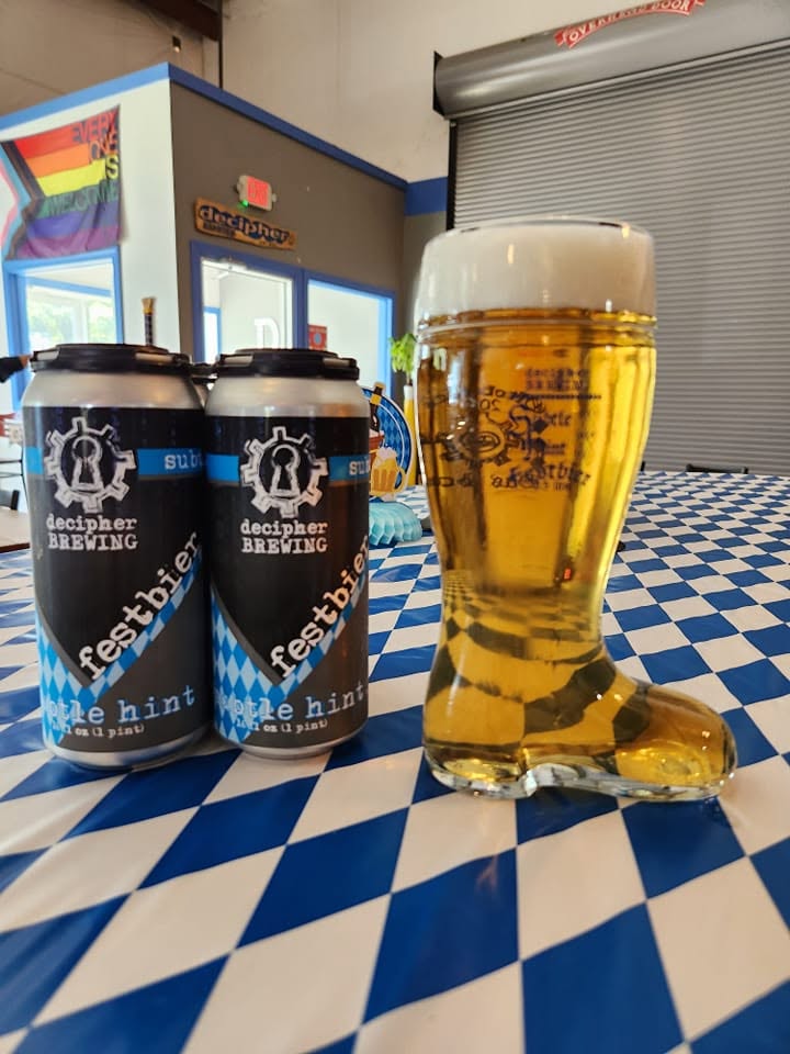 A glass of beer shaped like a sock and two cans of beer on a checkered table at a bar or brewery.