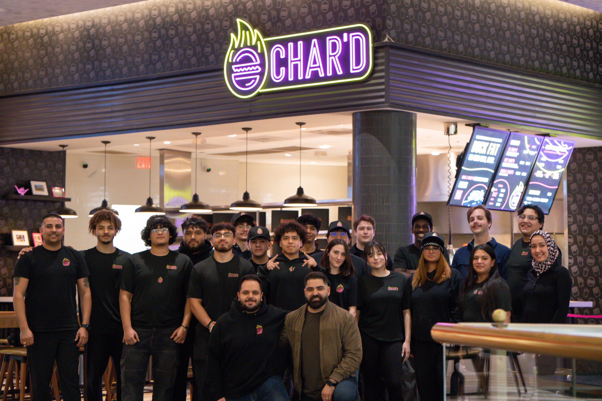 Group of people standing outside a restaurant with a purple sign that says 'CHAR'D'.