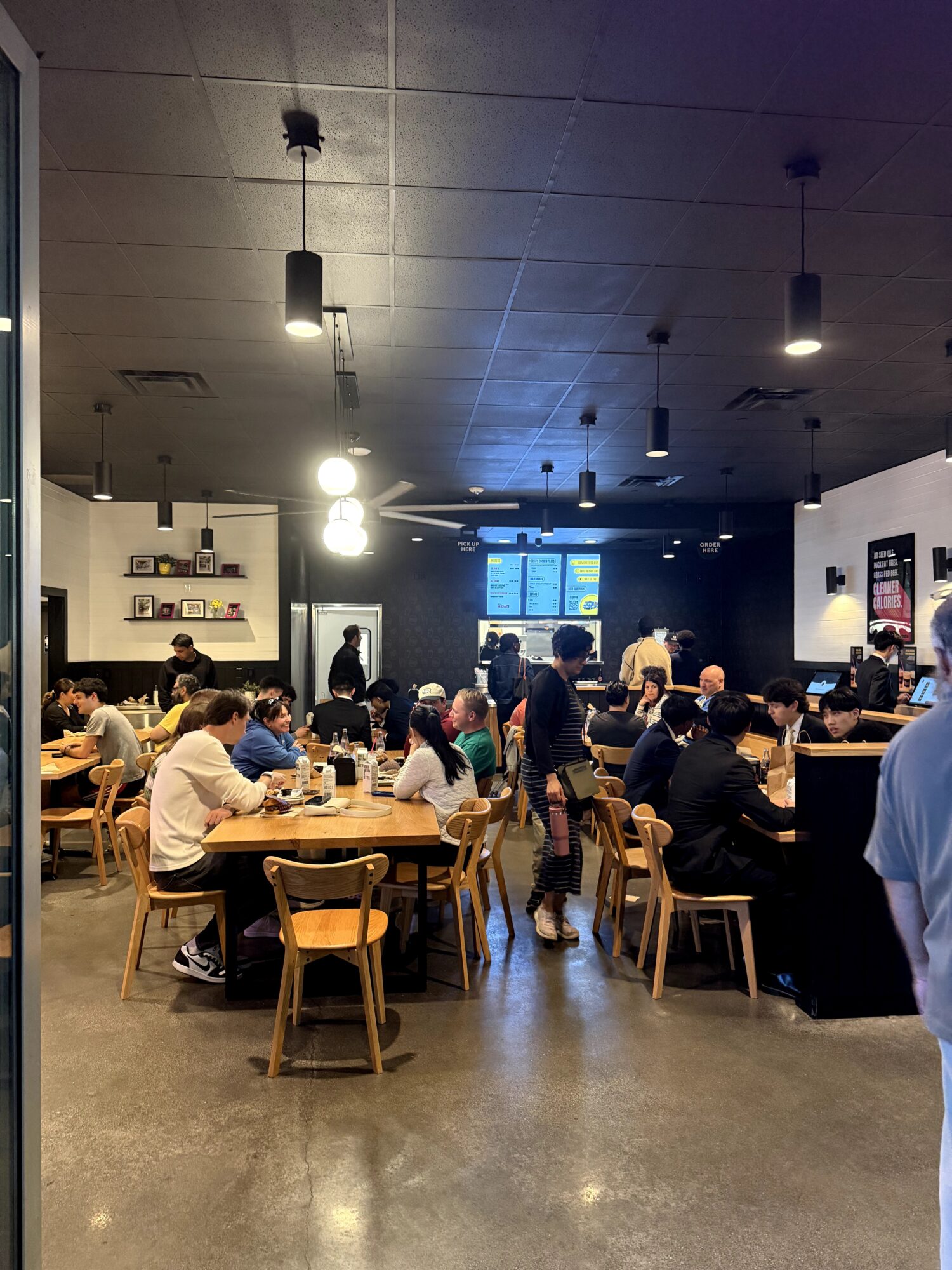 People sitting at tables in a busy cafe or restaurant, with a dark ceiling and ambient lighting, some standing and talking.