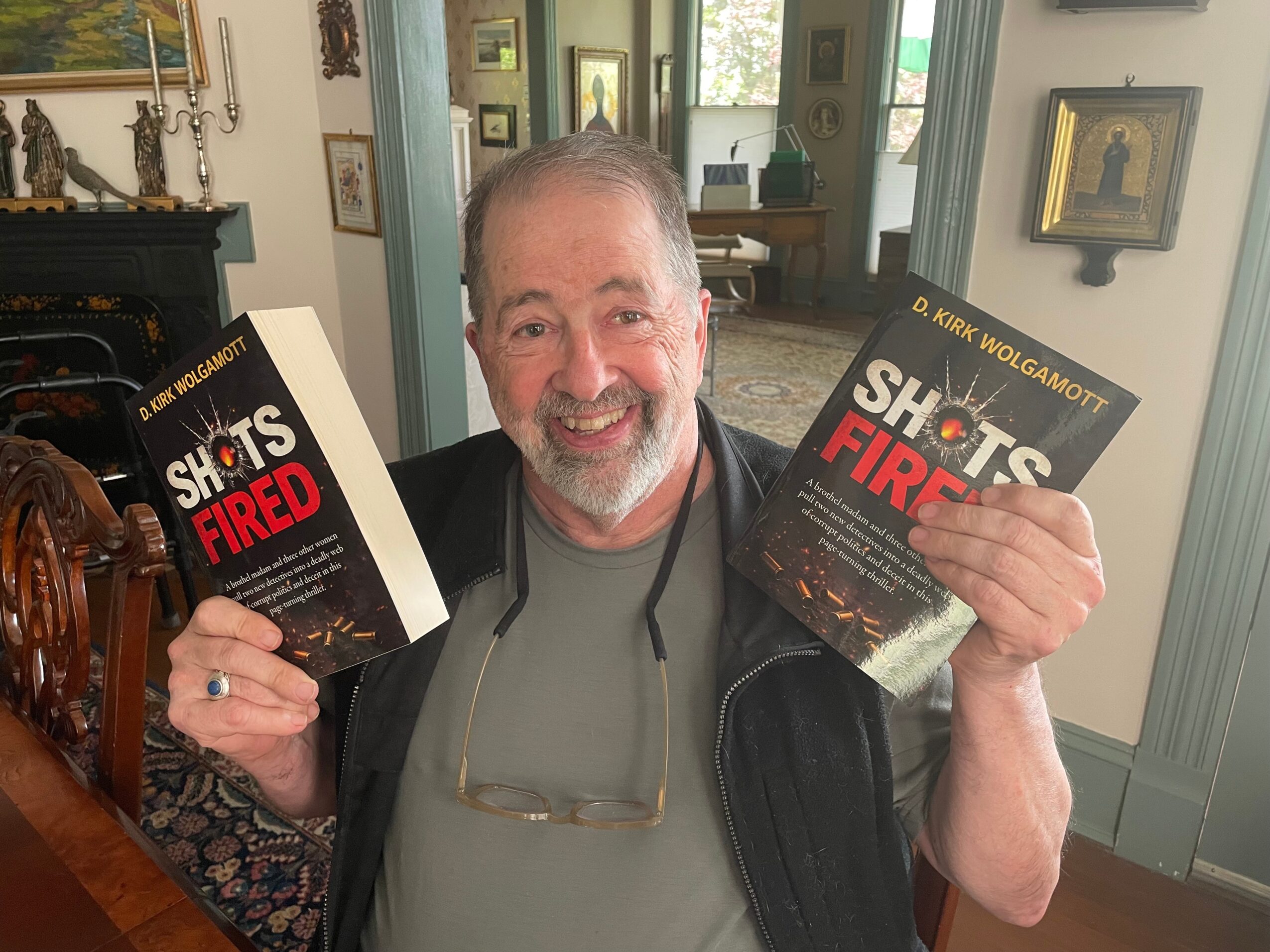Man holding two books titled 'Shit's Fired' in a room with framed pictures and a fireplace.