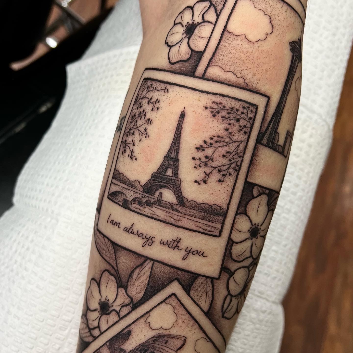 Tattoo of a Polaroid with the Eiffel Tower, surrounded by flowers, and the text 'I am always with you'.
