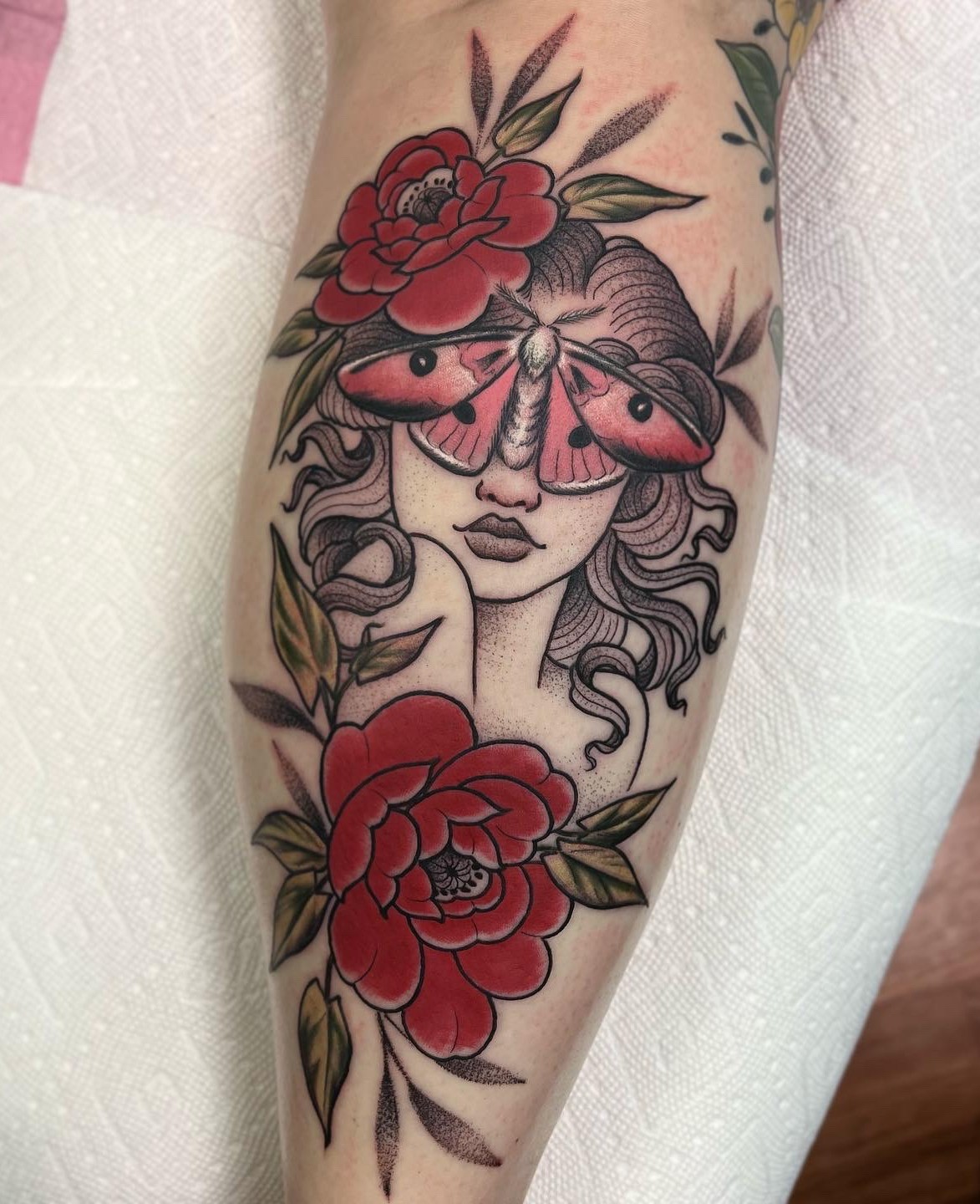 Tattoo of a woman's face with a butterfly and flowers, in black, red, and green colors.