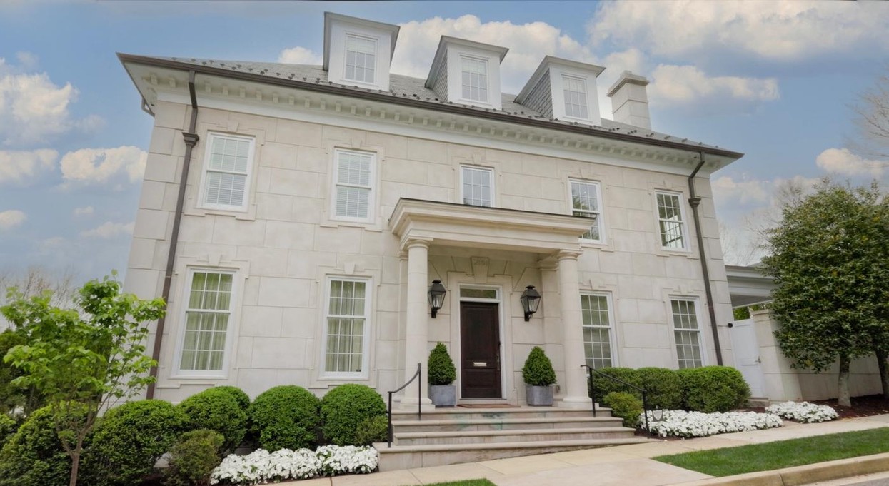 Large white house with multiple windows, a central entrance with steps, and landscaped front yard with bushes and flowers.