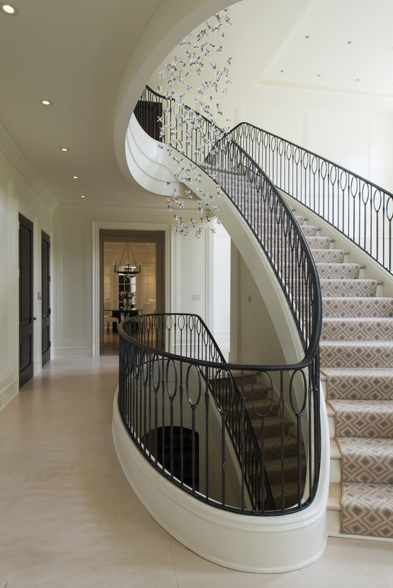 Spiral staircase with black railing and carpeted steps inside a modern building, with a hallway and doorway in the background.