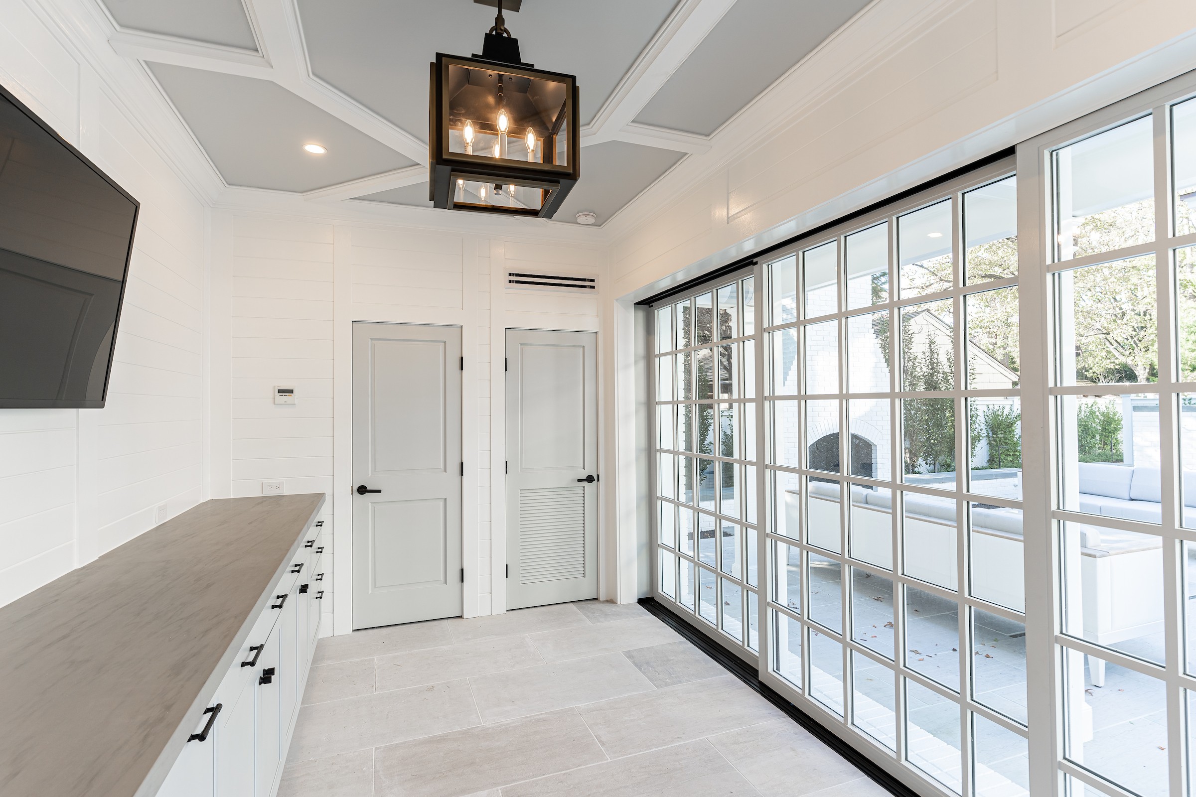 Bright room with large glass block wall, white walls, ceiling, and cabinetry, and a mounted TV, with a view outside.