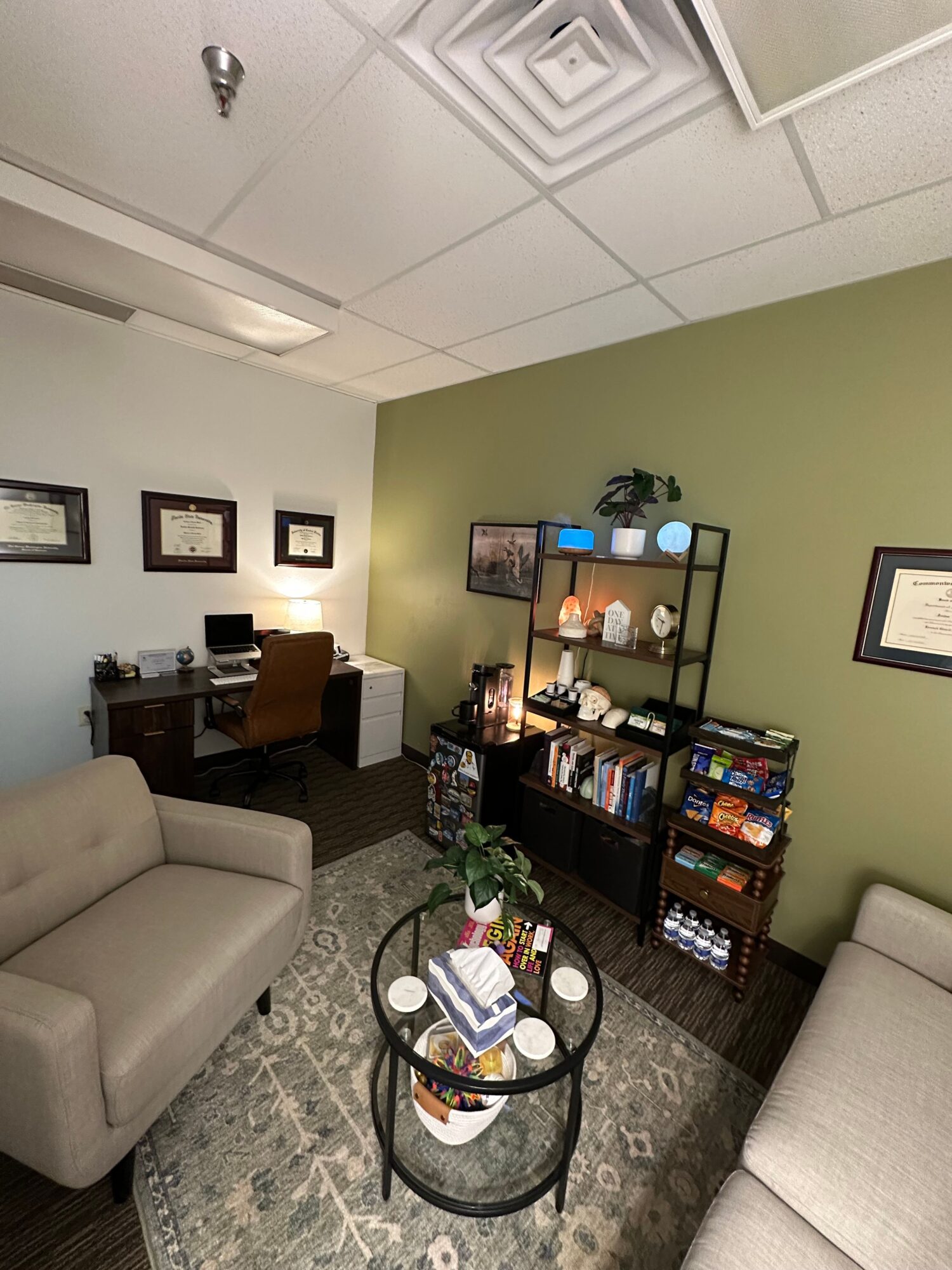 Living room with green and white walls, bookshelf, desk, and beige sofa, viewed from the side.