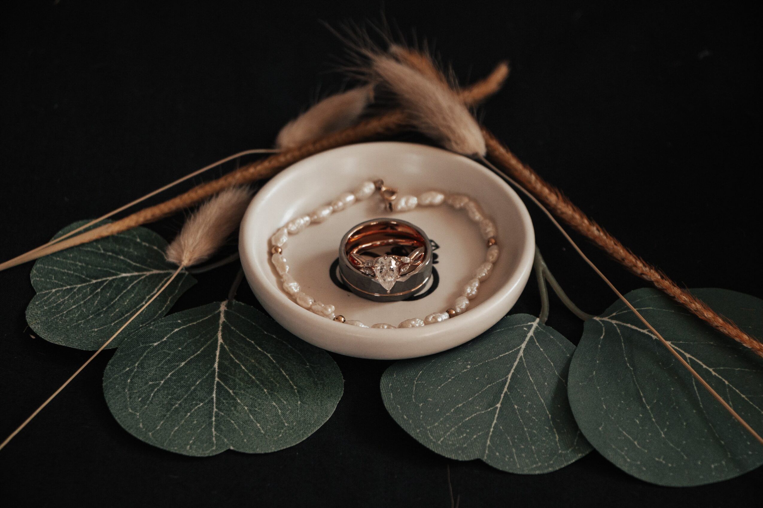 Ring on a small dish surrounded by green leaves and decorative elements, set against a dark background.