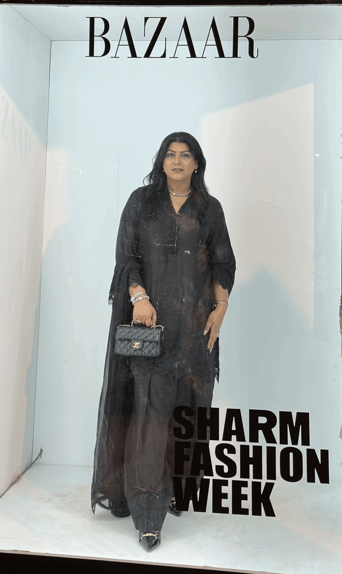 Woman in black outfit holding a handbag, standing in front of a light blue background with text about fashion week.