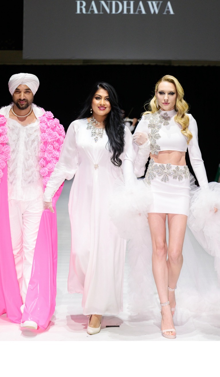 Three models walk on runway, two women in white outfits and a man in pink and white, with 'RANDHWA' displayed above.