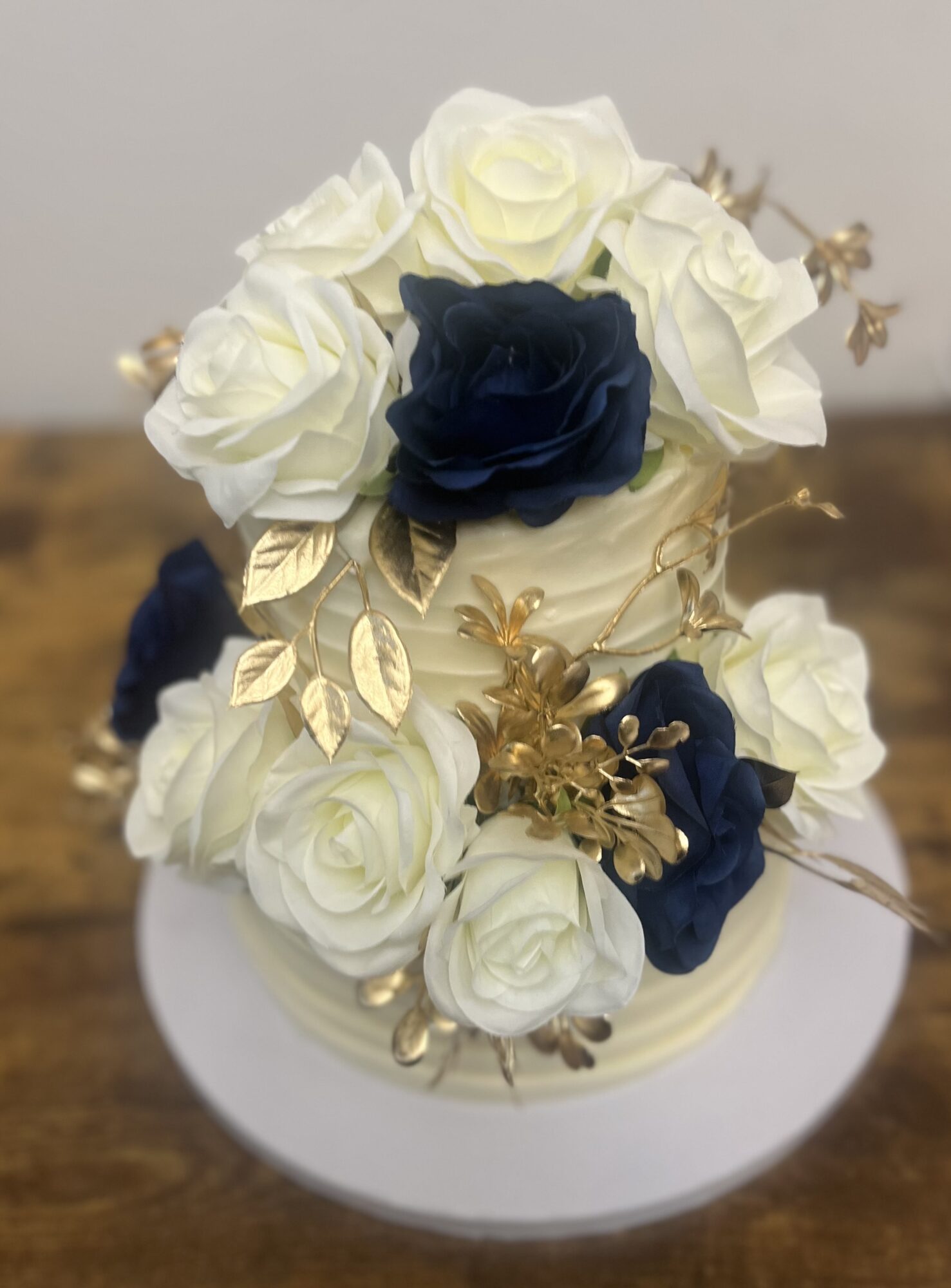 A floral arrangement with white and dark blue roses, gold leaves, and decorative gold accents on a white base.