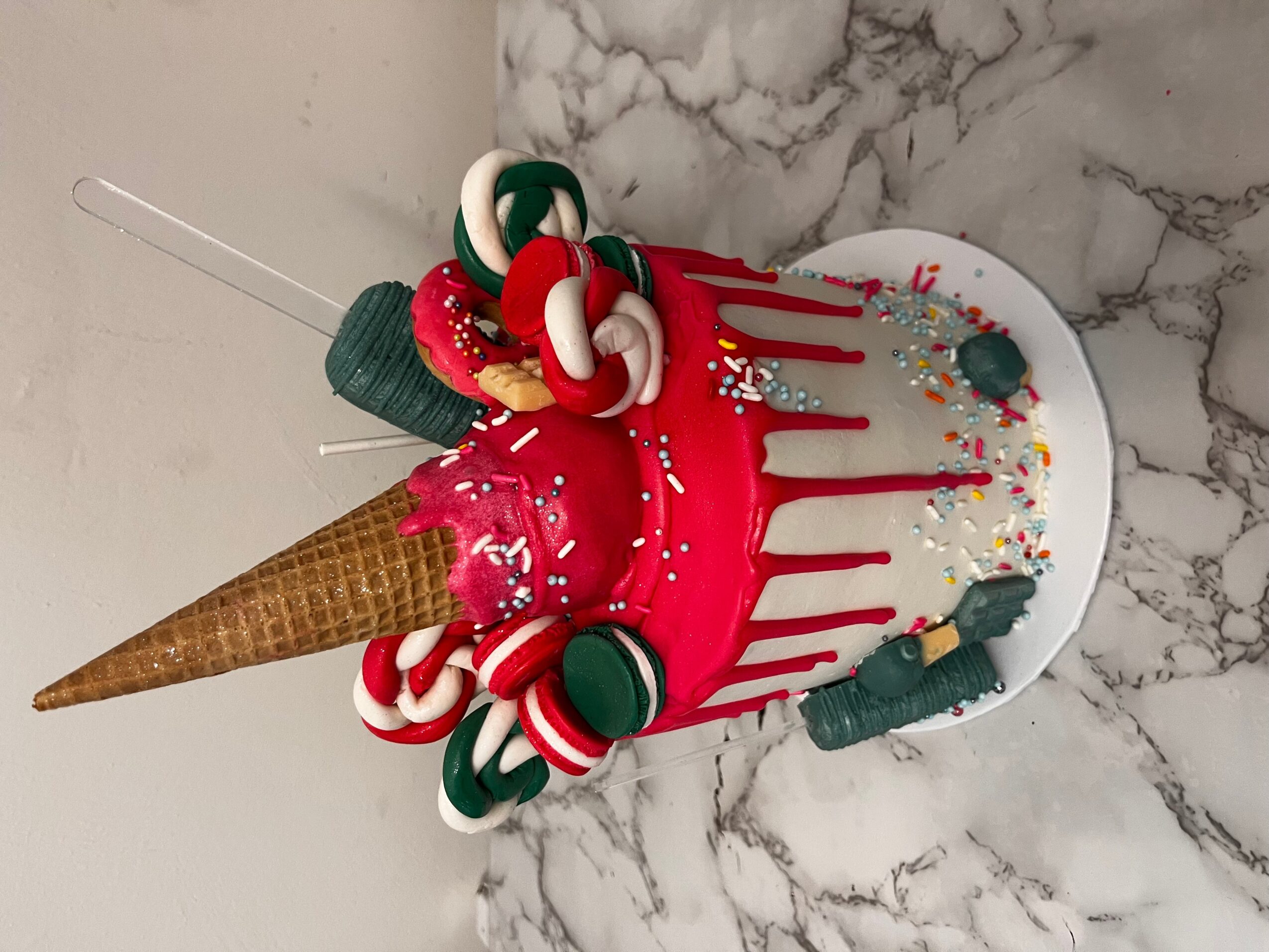 Cake with red dripping icing, candy canes, and an ice cream cone on a marble surface.
