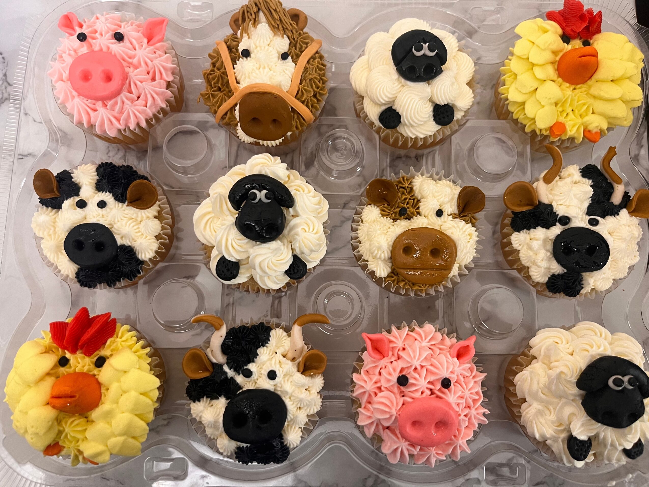 Collection of cupcakes decorated as farm animals, including pig, cow, sheep, duck, and horse, with colorful frosting and details.