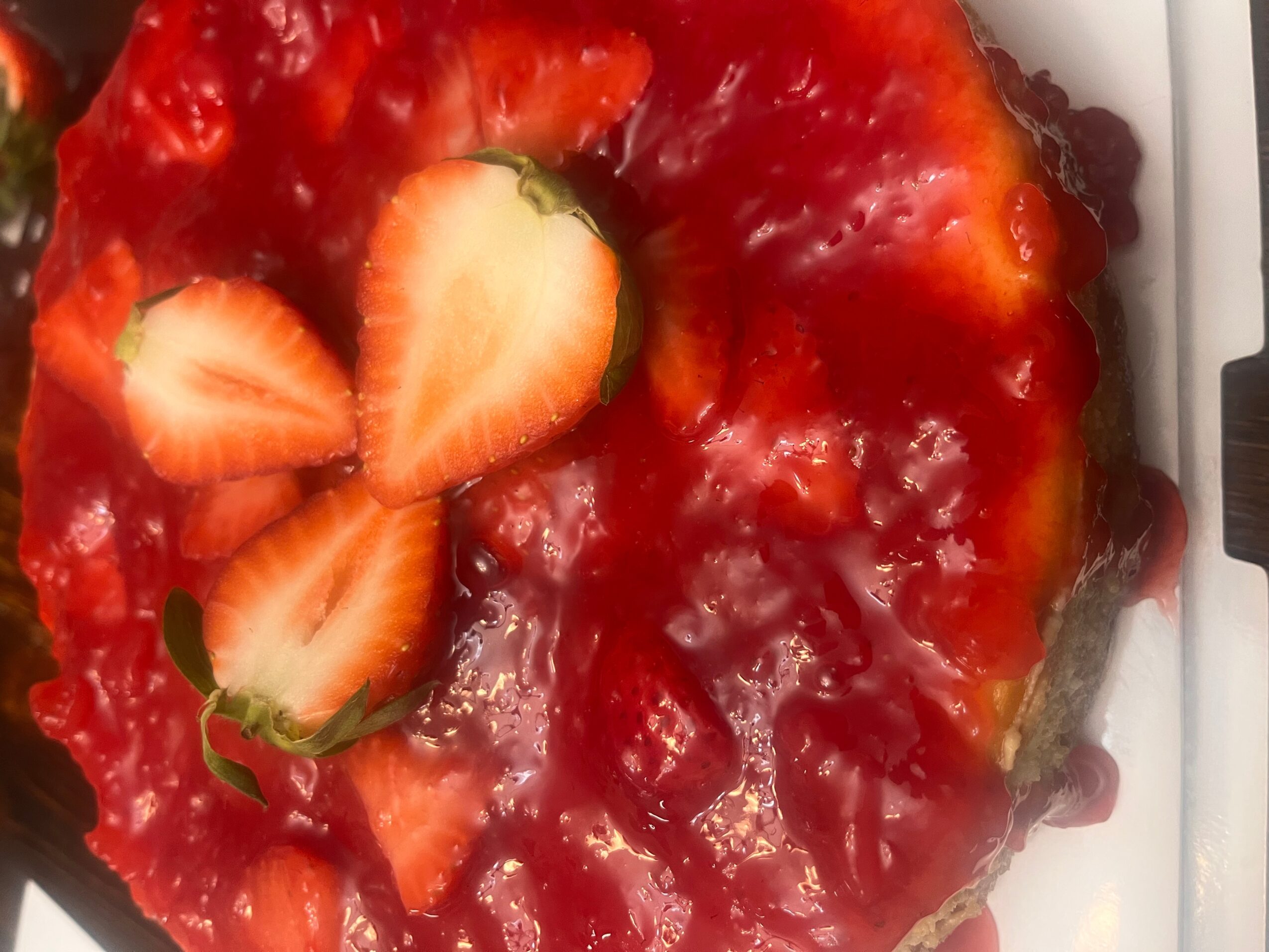 Strawberry cake with sliced strawberries on top, showing red glaze and cake layers, on a white surface.