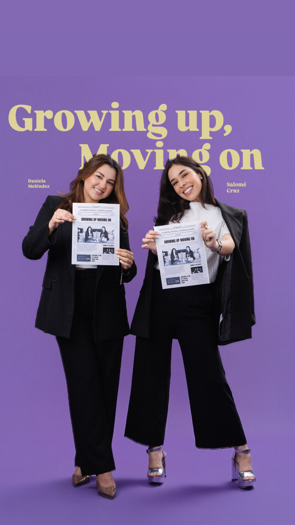 Two women in black suits holding newspapers, smiling, standing against a purple background with large yellow text.