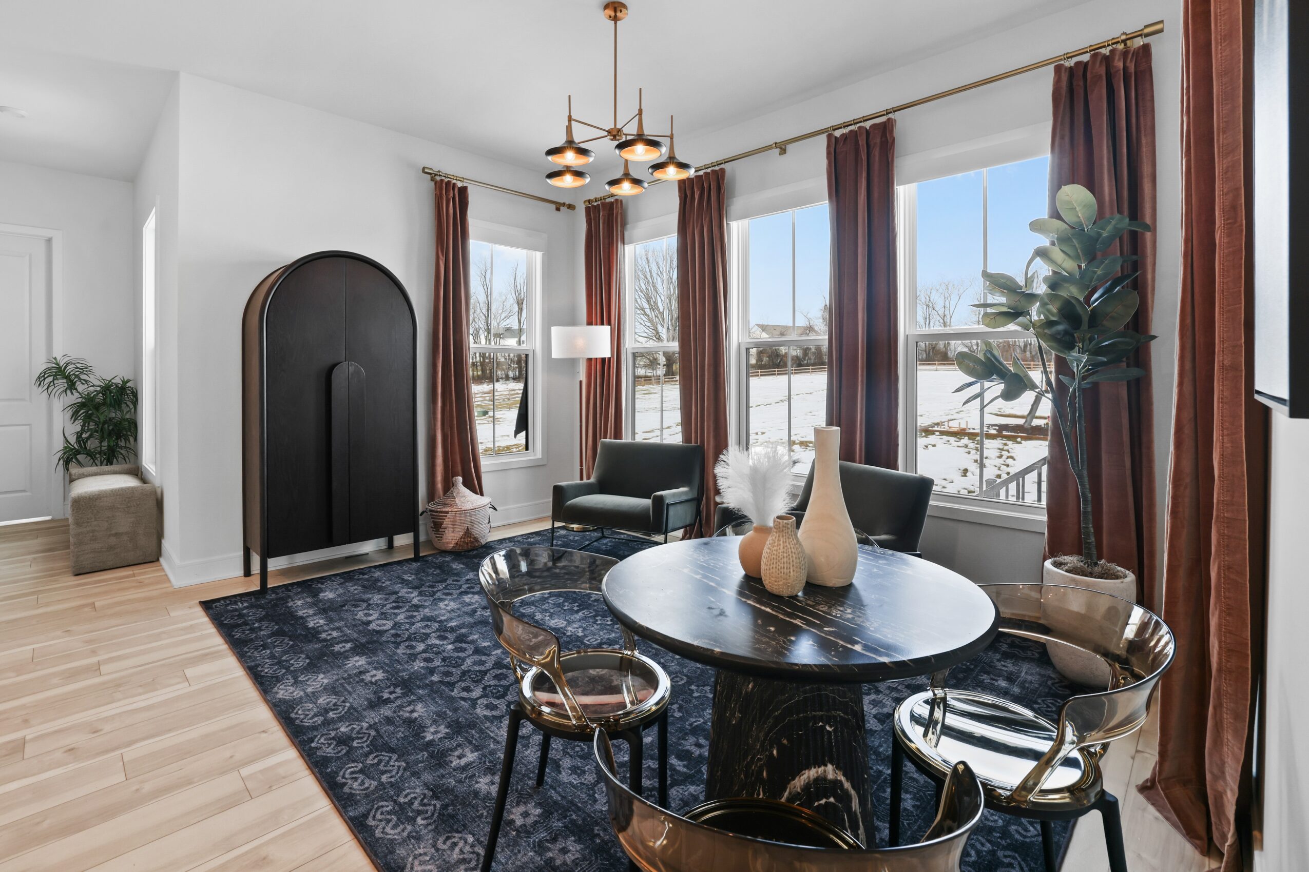 Living room with round black dining table, four chairs, large windows with curtains, chandelier, and a blue rug.