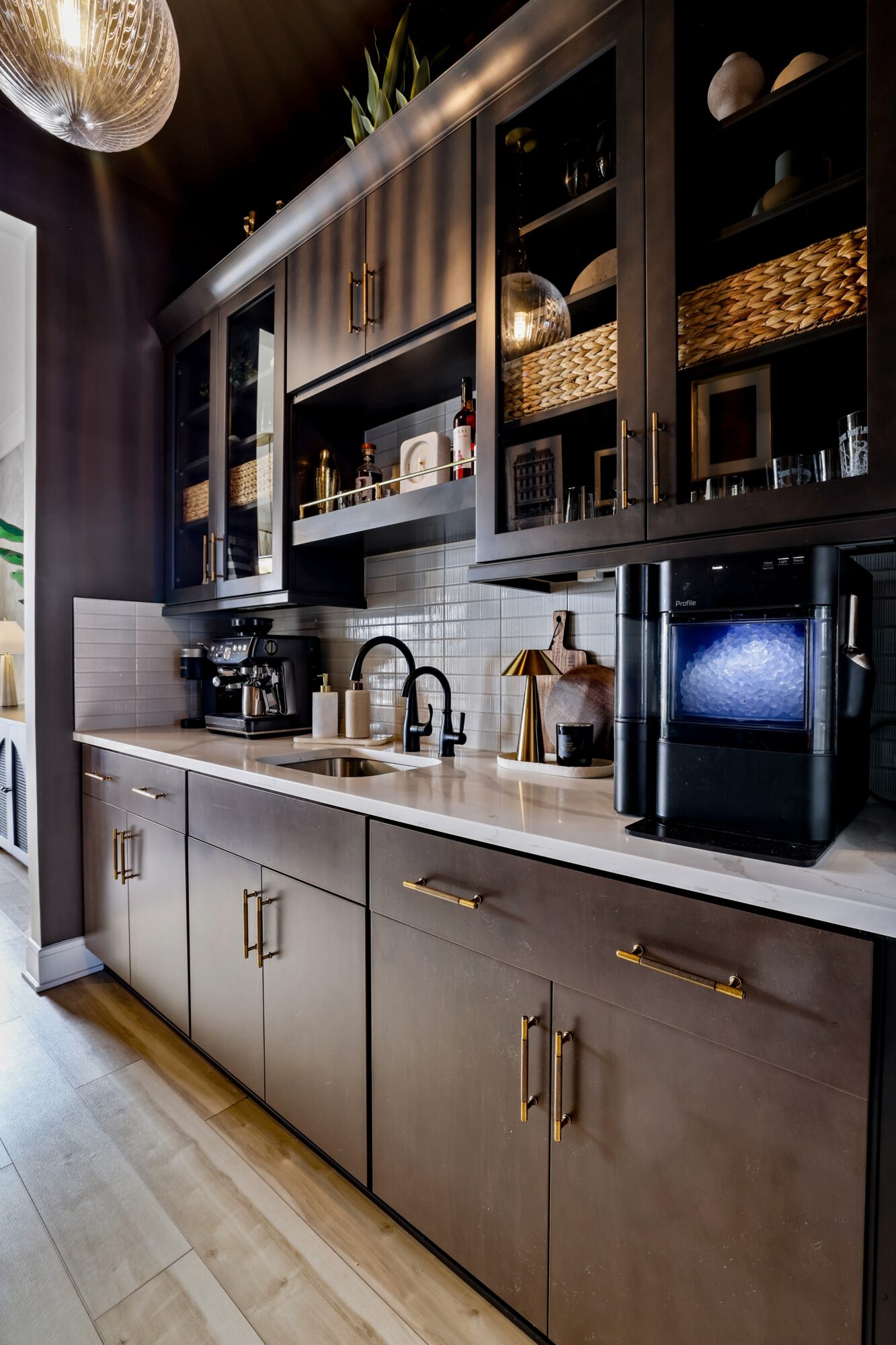 Kitchen with black upper cabinets, white countertop, and lower cabinets with gold handles, coffee machine, microwave, and sink.