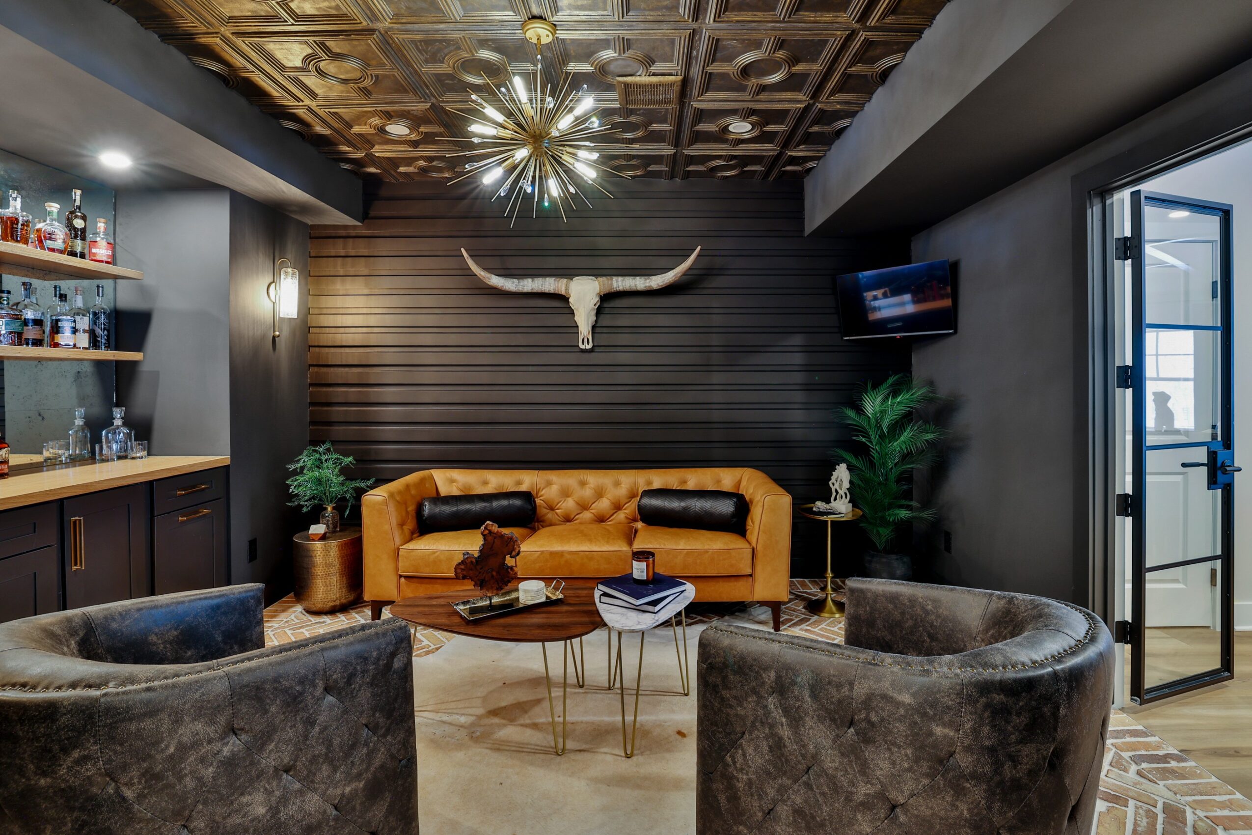 Living room with a yellow sofa, two gray armchairs, a wooden coffee table, and decorative plants, with a bull skull on the wall.