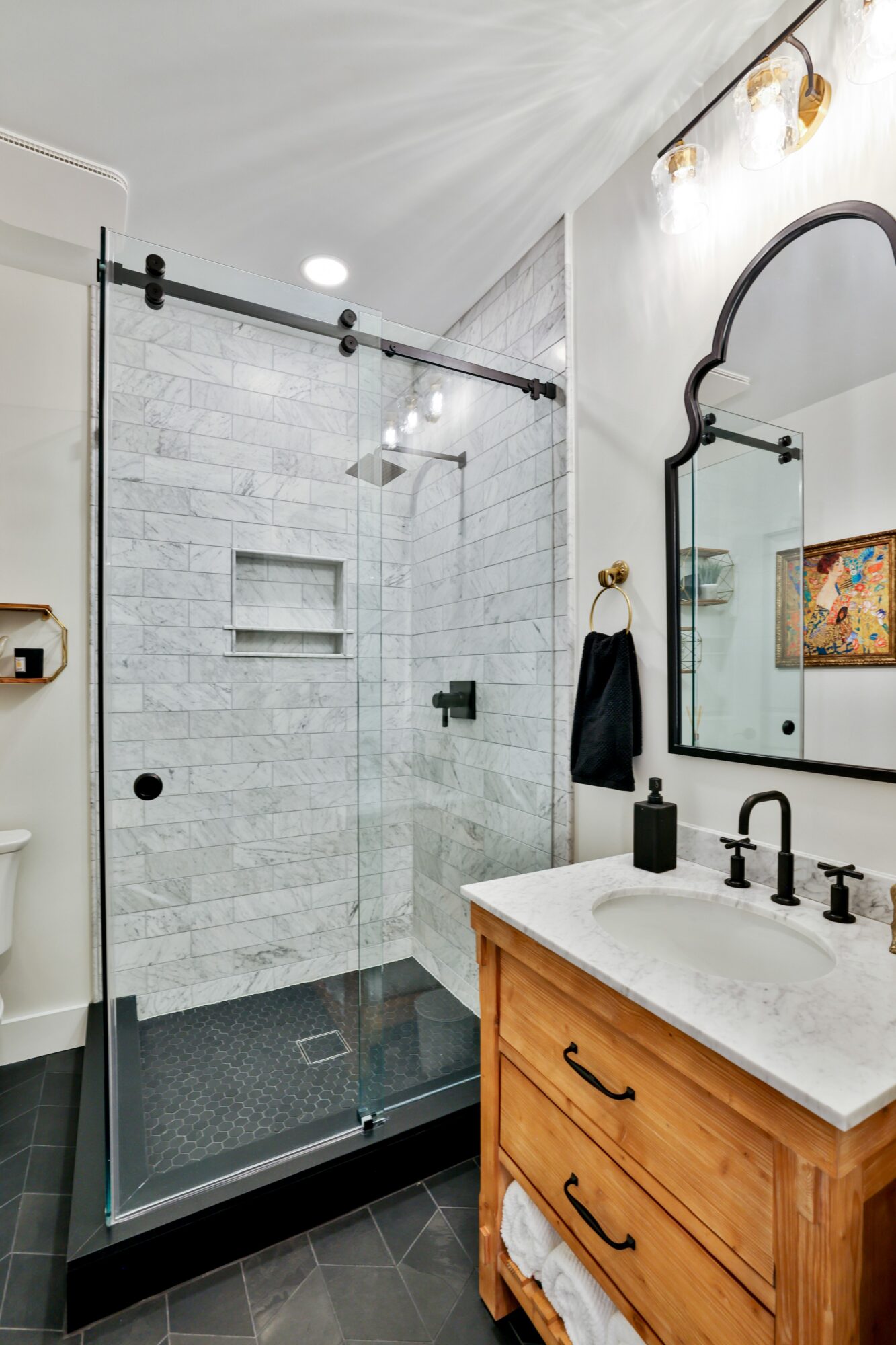 Bathroom with glass shower enclosure, white tiled walls, wooden vanity with a white countertop, and a large mirror.