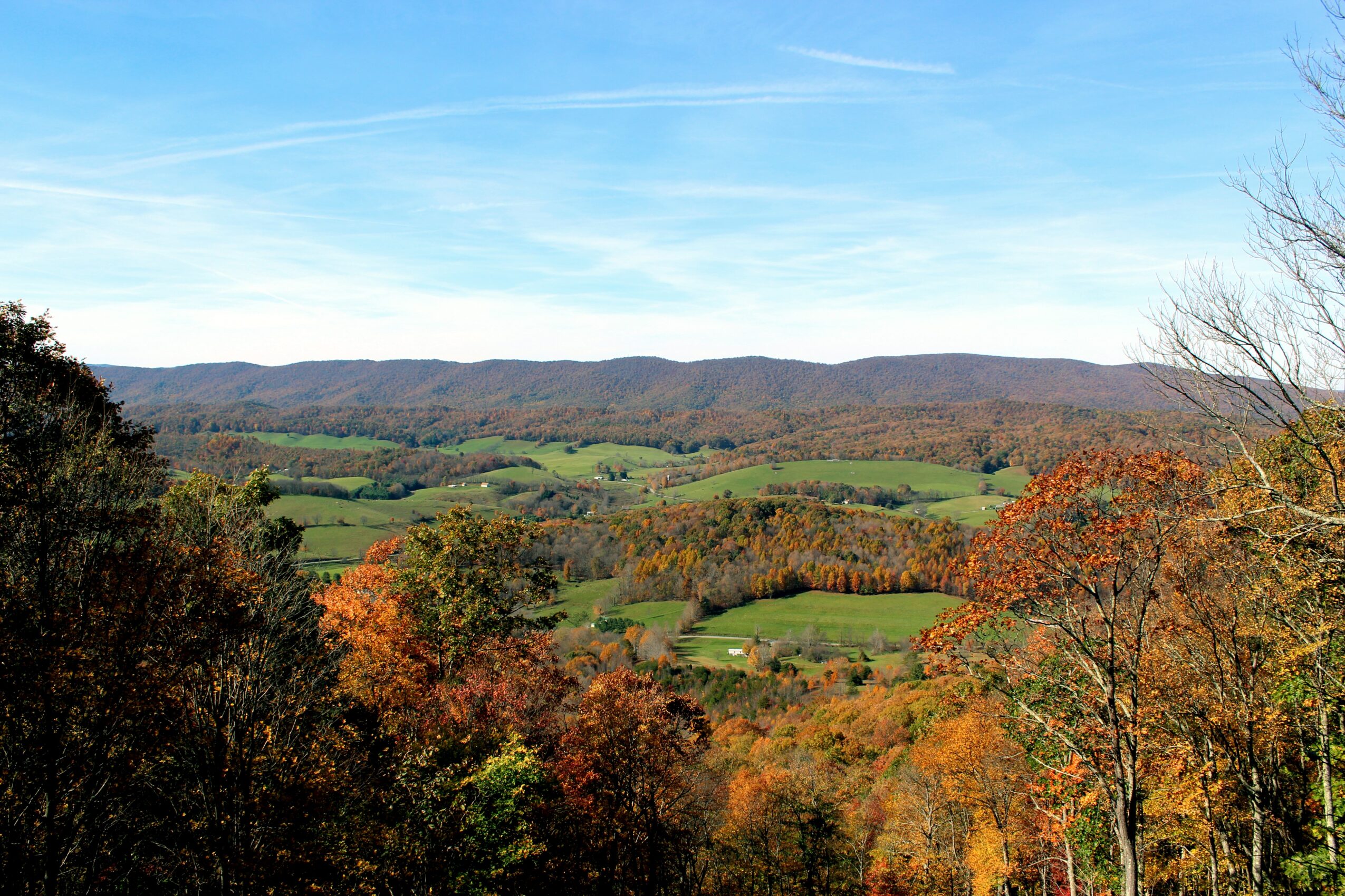 Scenic landscape with rolling hills, trees with autumn foliage, and a blue sky with wispy clouds.