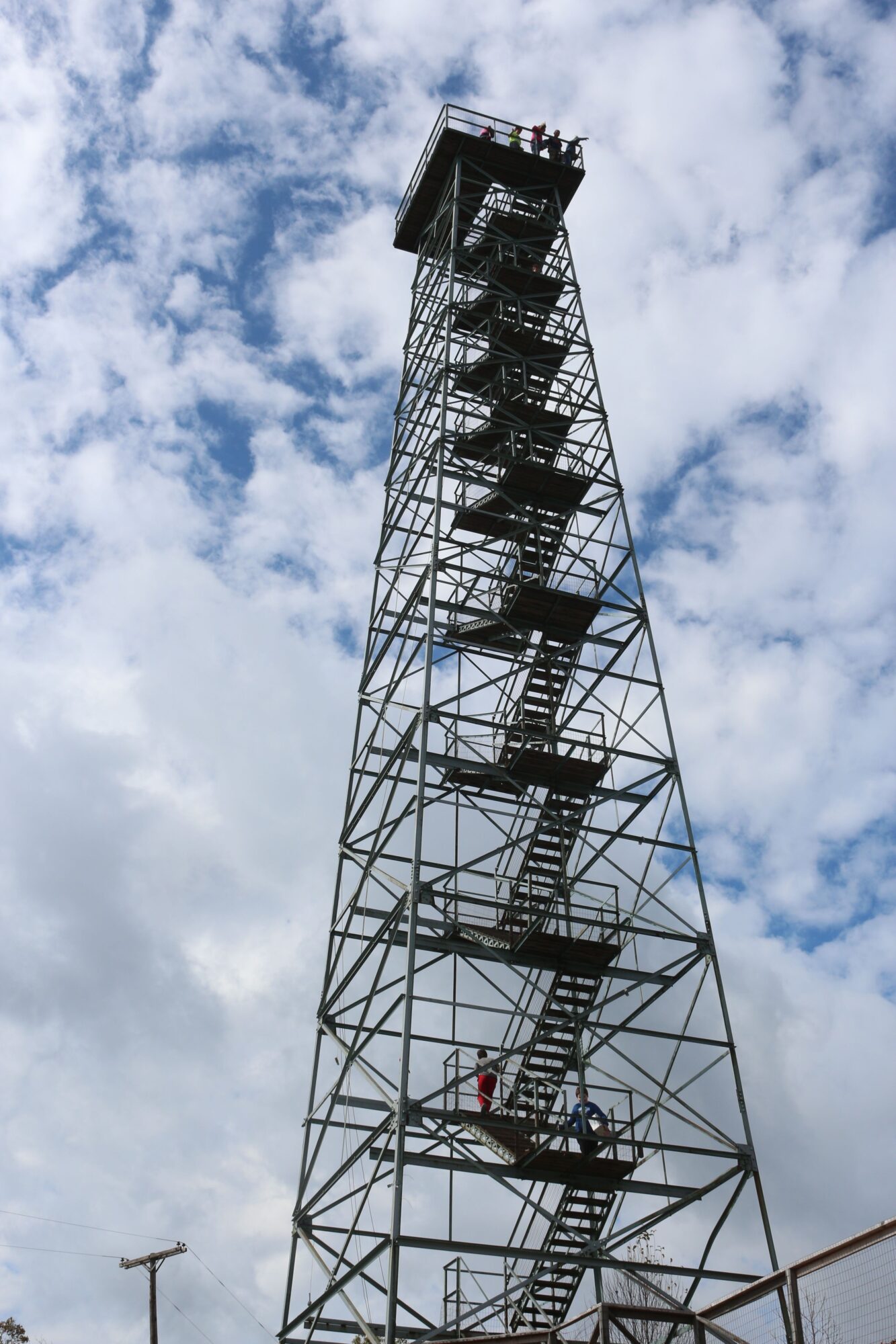 Tall radio tower with antennas against a partly cloudy sky, viewed from below.
