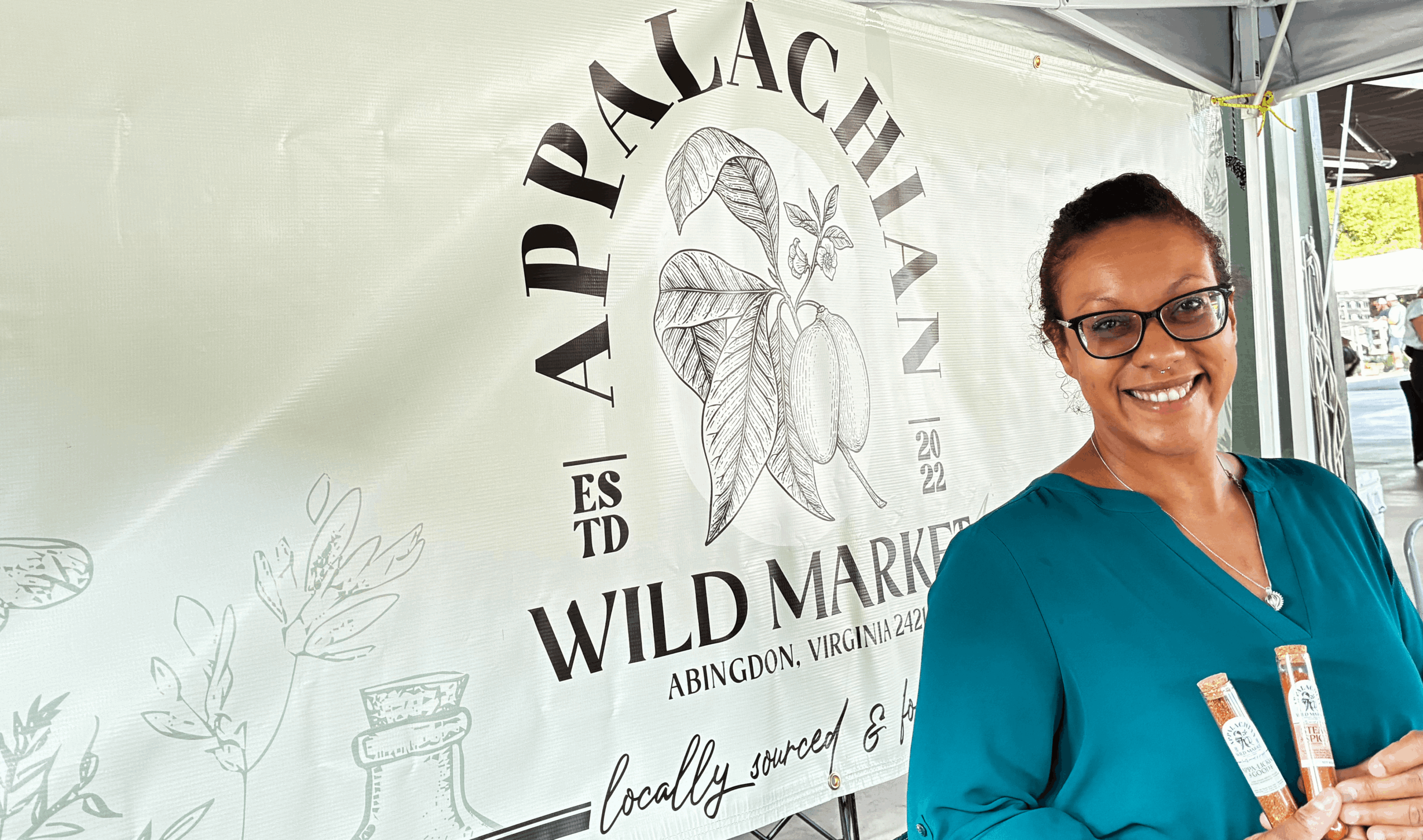 Smiling woman with glasses and blue shirt standing in front of a banner with a bird logo and text.