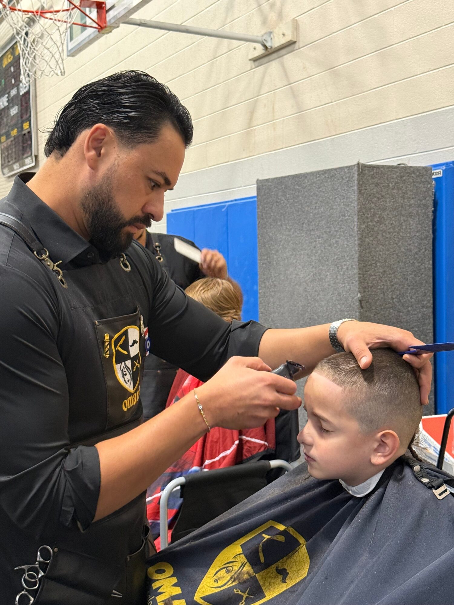 A police officer with dark hair and beard interacts with a young boy with short hair, in a room with blue and gray walls.