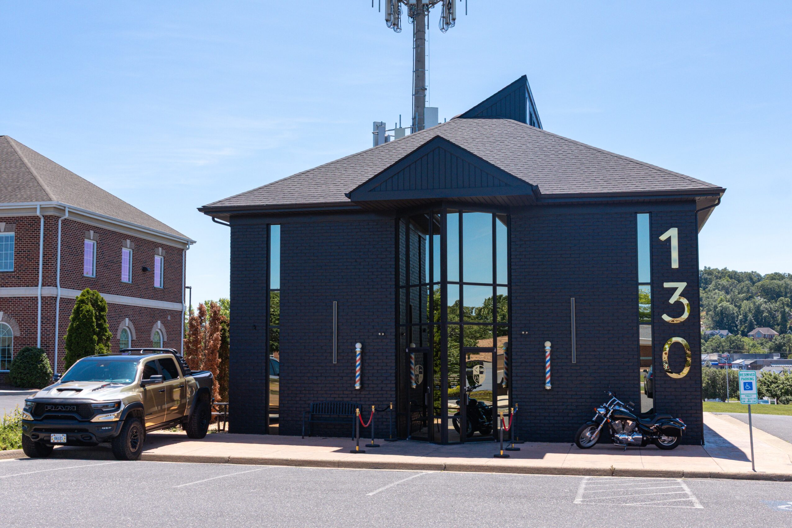 Modern black building with large glass entrance, numbers 130 on the side, parked car and motorcycle outside, blue sky.