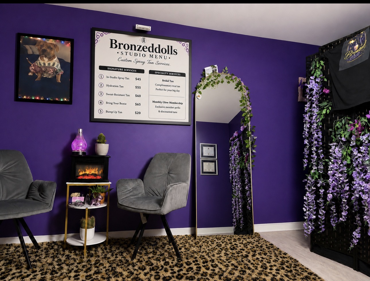 Purple wall with a sign, two chairs, a small table with plants, and a floral archway in a studio setting.