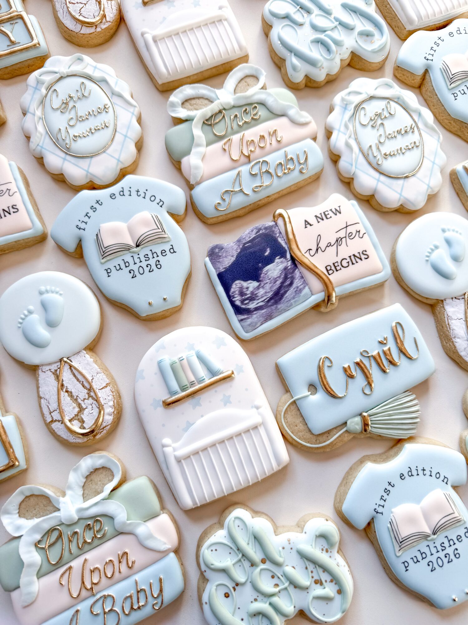 Assorted decorated cookies with baby-themed messages and images, including a mountain landscape, a gift box, and text like