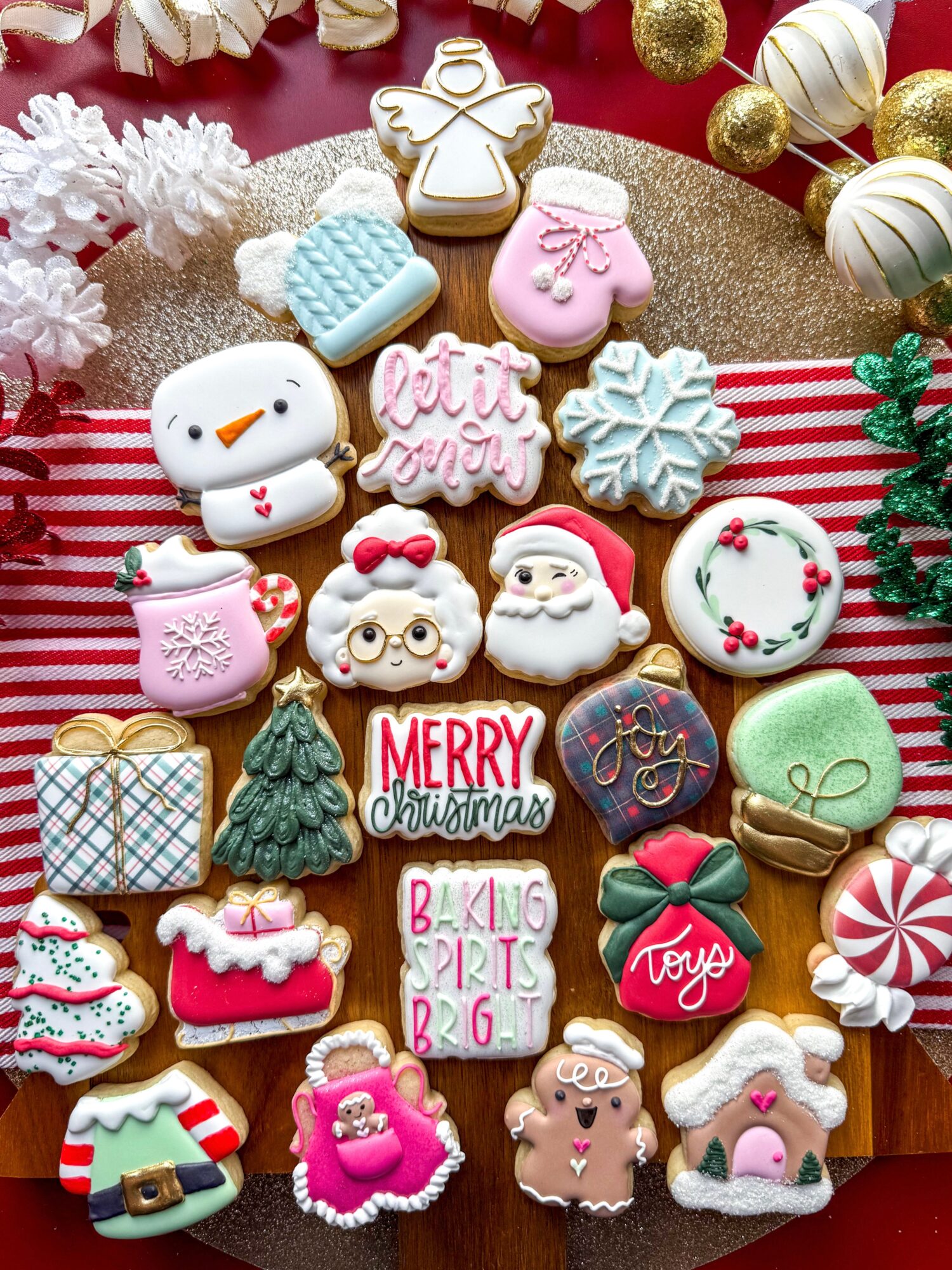 Assorted Christmas cookies with festive decorations on a striped cloth, including snowmen, trees, Santa, and gift-shaped cookies.