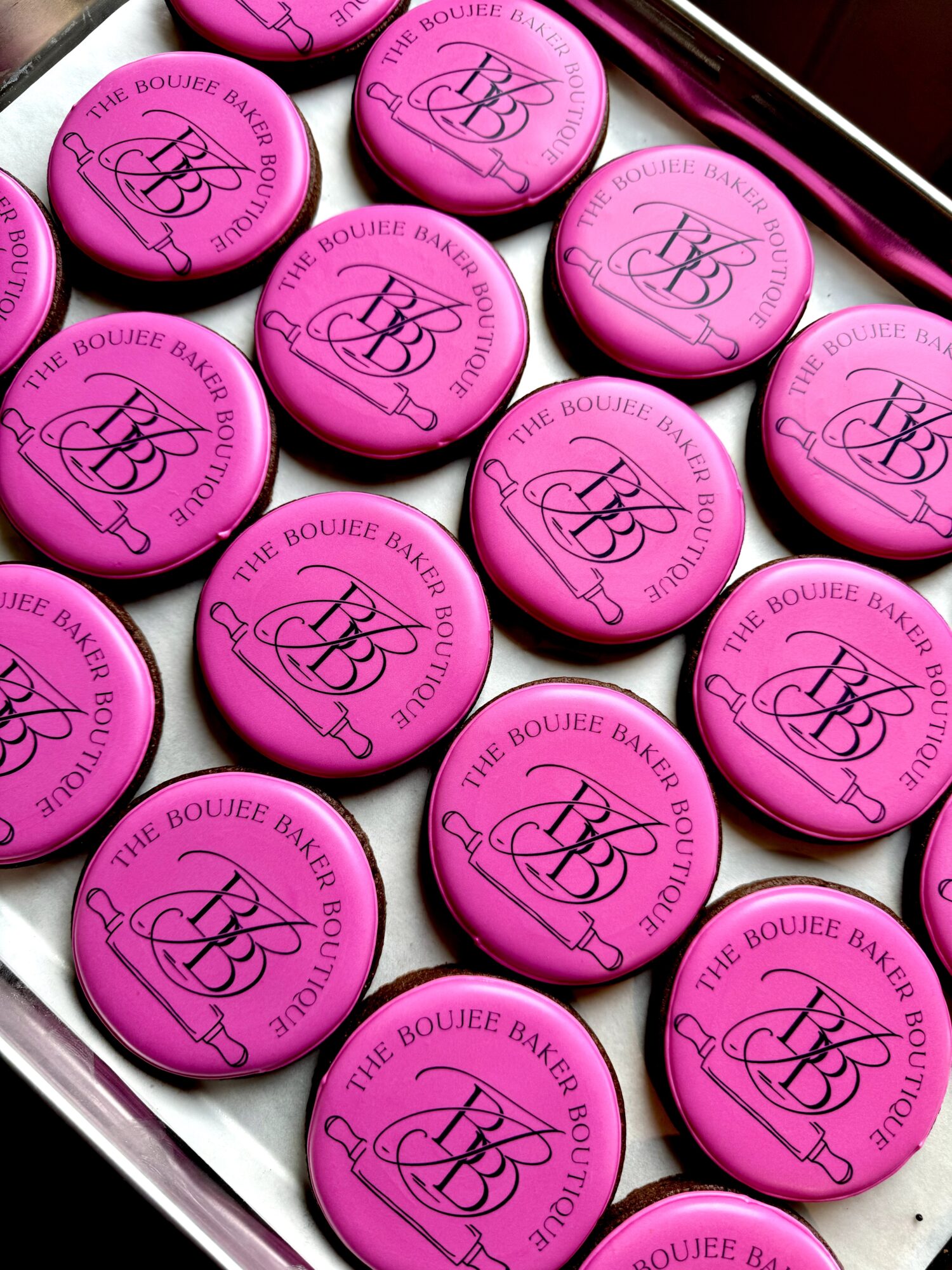 Pink round makeup compacts with black logo and text, arranged in a grid inside a metallic case.