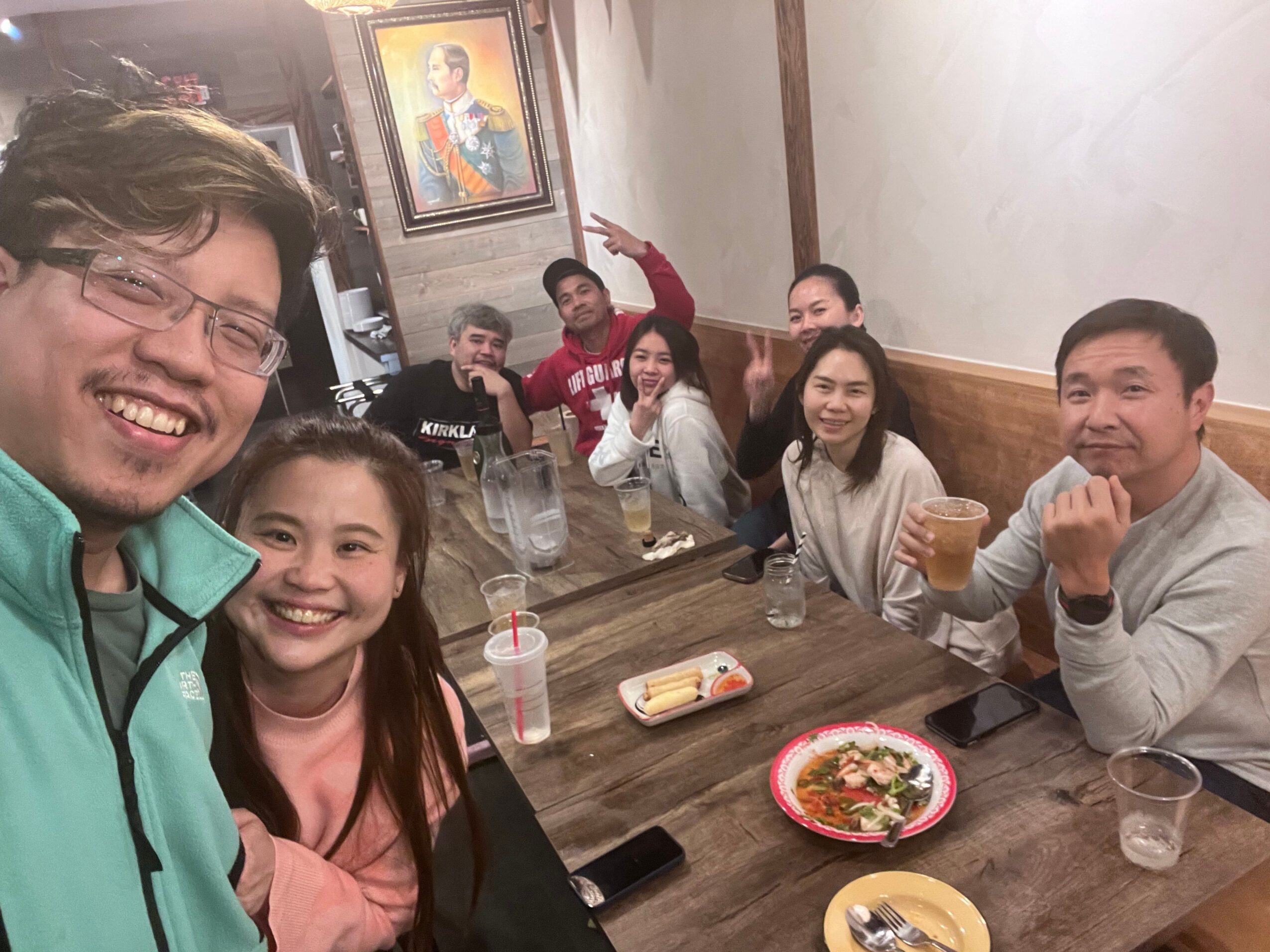 Group of people smiling and sitting at a table with food and drinks, indoors.