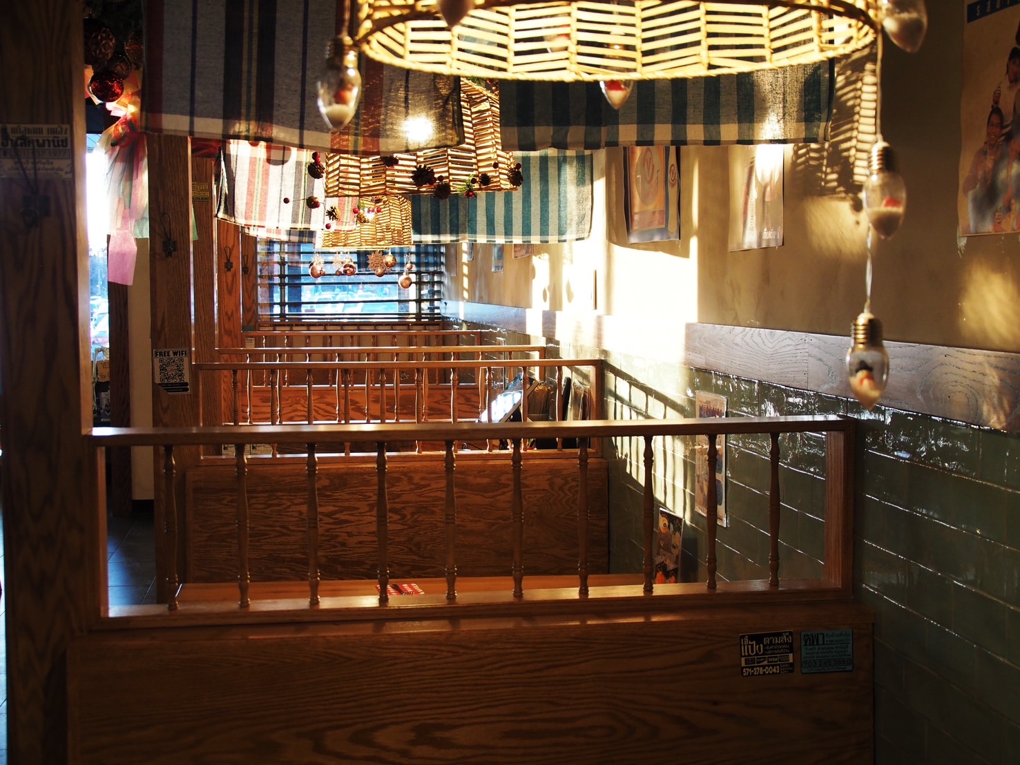 Indoor space with wooden railing, hanging lights, and colorful fabric decorations, illuminated by natural light from windows.