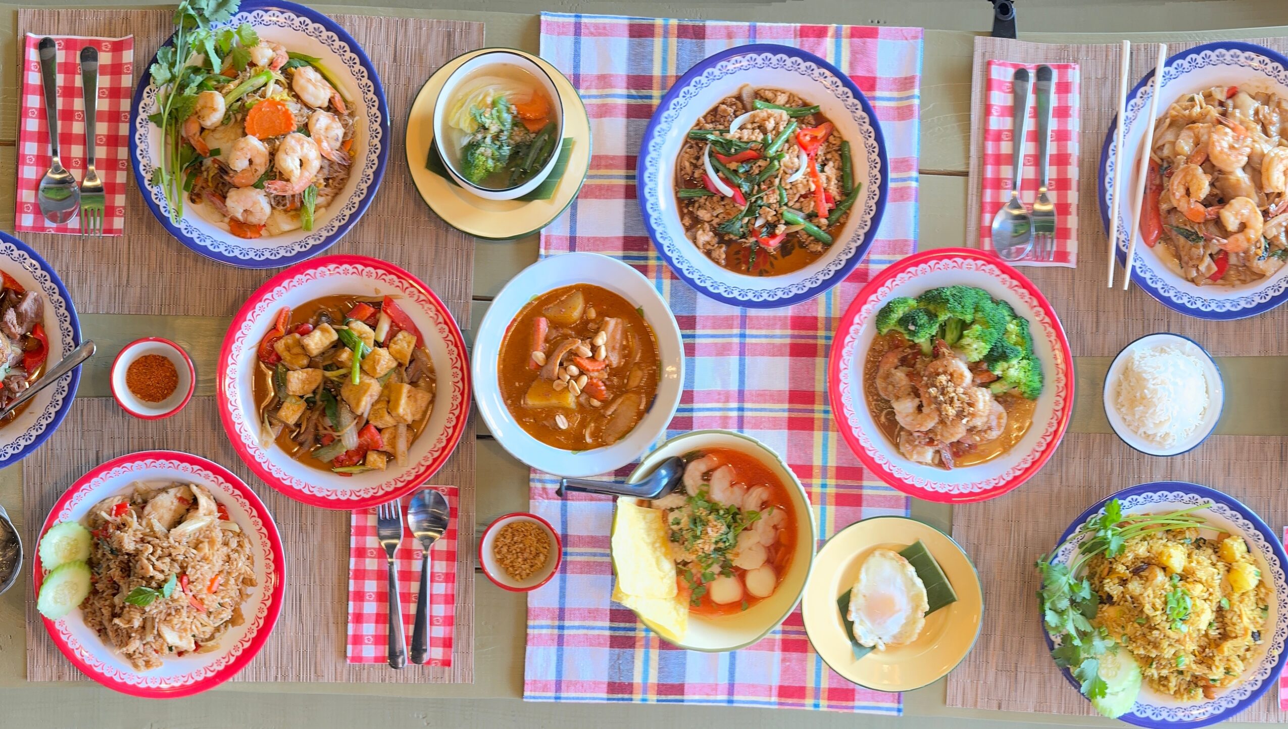 Table with various dishes, bowls, and drinks on a checkered tablecloth, viewed from above.