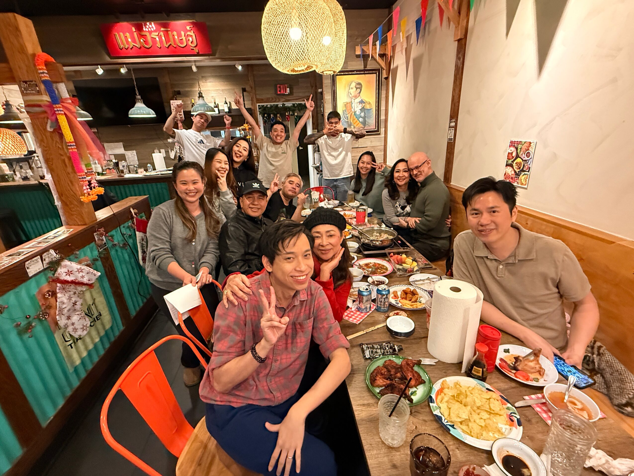 Group of people gathered around a long table in a decorated restaurant, smiling and celebrating, with food and drinks on the table.
