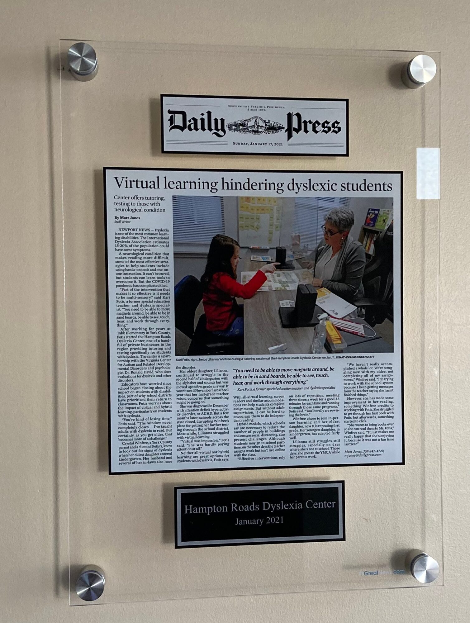 Newspaper article about dyslexia students with a woman and a man at a desk, on a wall with a sign above and a plaque below.