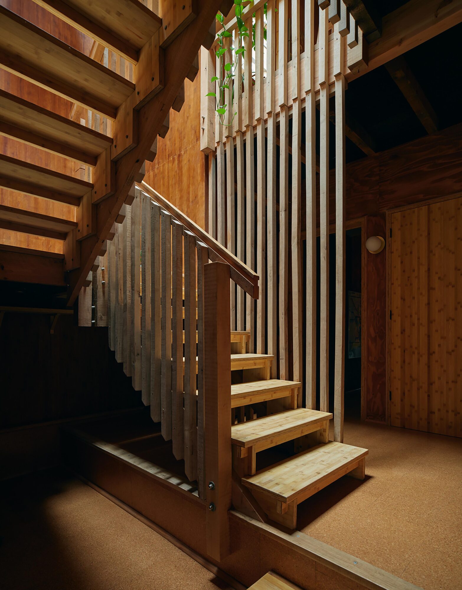Wooden staircase with vertical slats and railing inside a cabin-like space, with wooden walls and ceiling, and a carpeted floor.