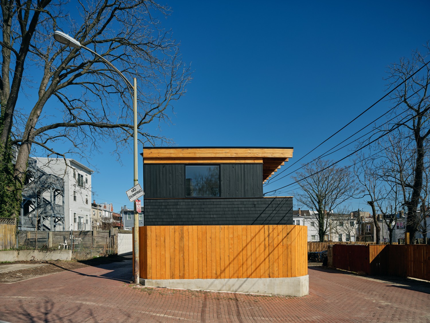 Small modern building with black and wooden exterior, trees, and a clear blue sky in the background.