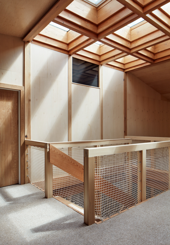 Interior space with wooden ceiling panels and a mesh-fenced enclosure, illuminated by natural light from skylights.