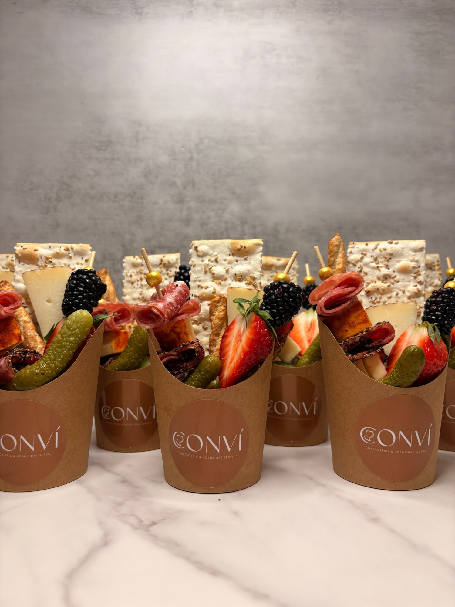 Three cups of dessert topped with strawberries, blackberries, and slices of kiwi, with cake pieces in the background on a marble surface.