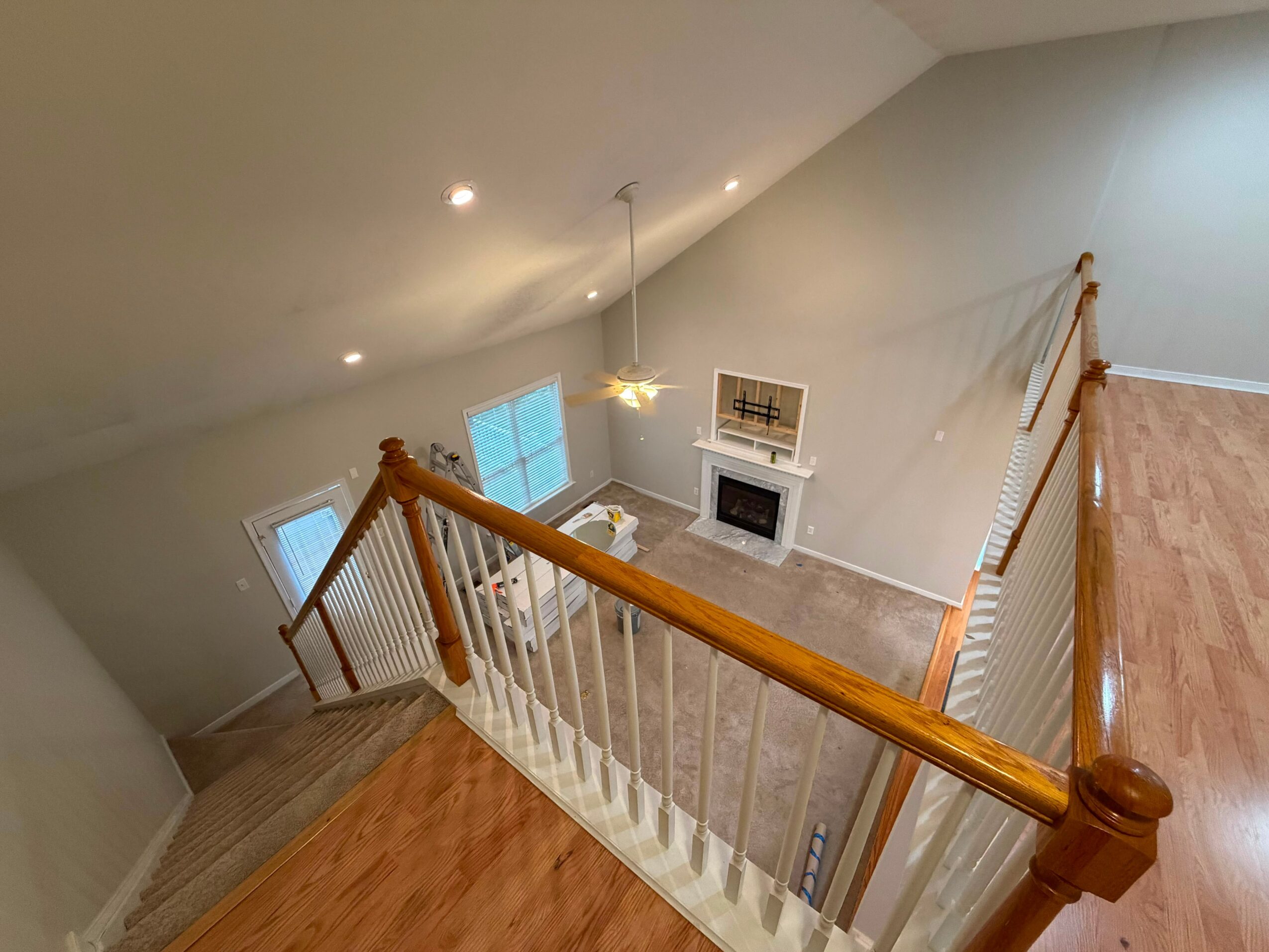View from the staircase looking down into a living room with a fireplace, windows, and a ceiling light fixture.