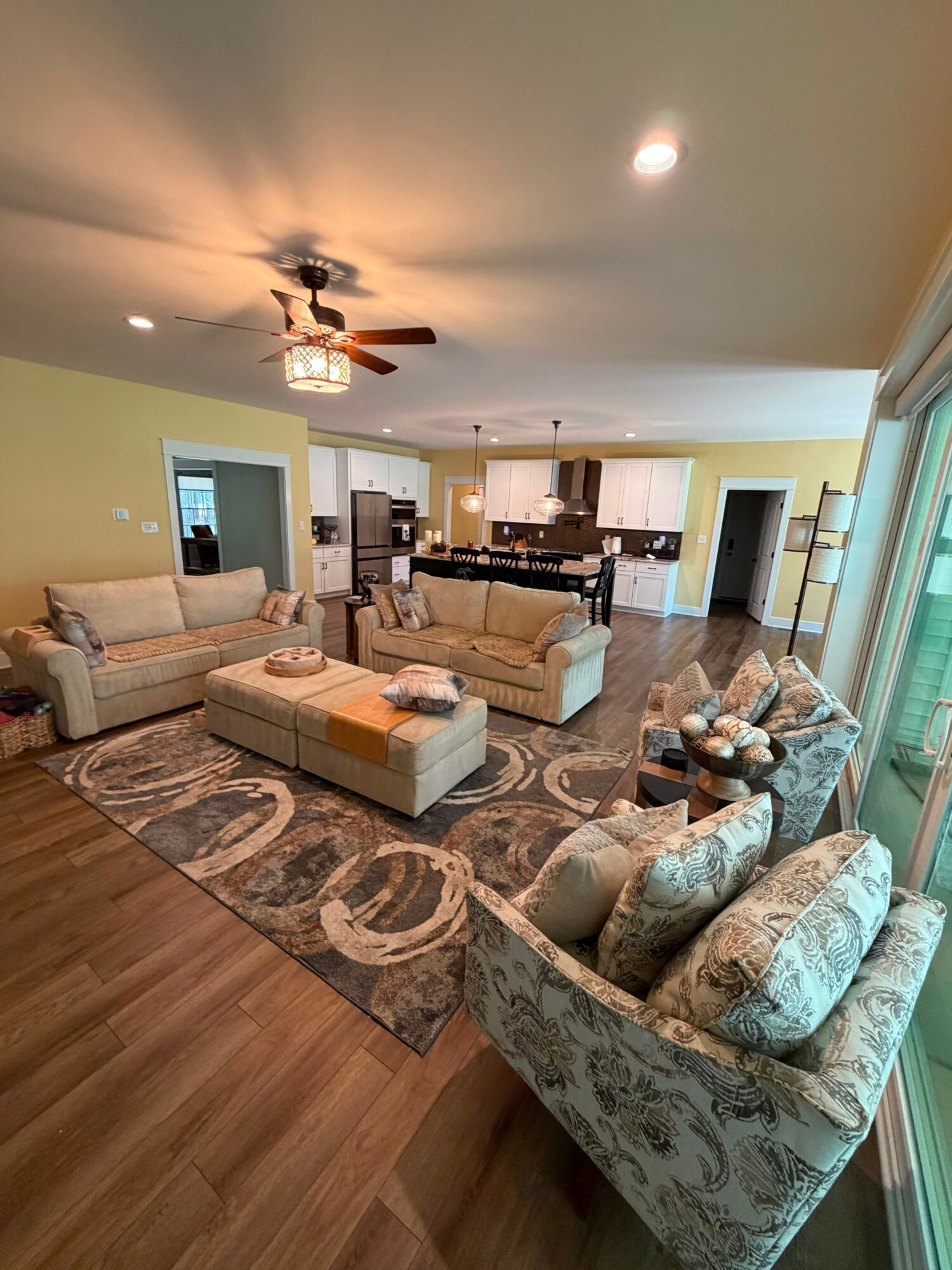 Living room with two sofas, a patterned armchair, a coffee table, and a rug, with a ceiling fan and large window.