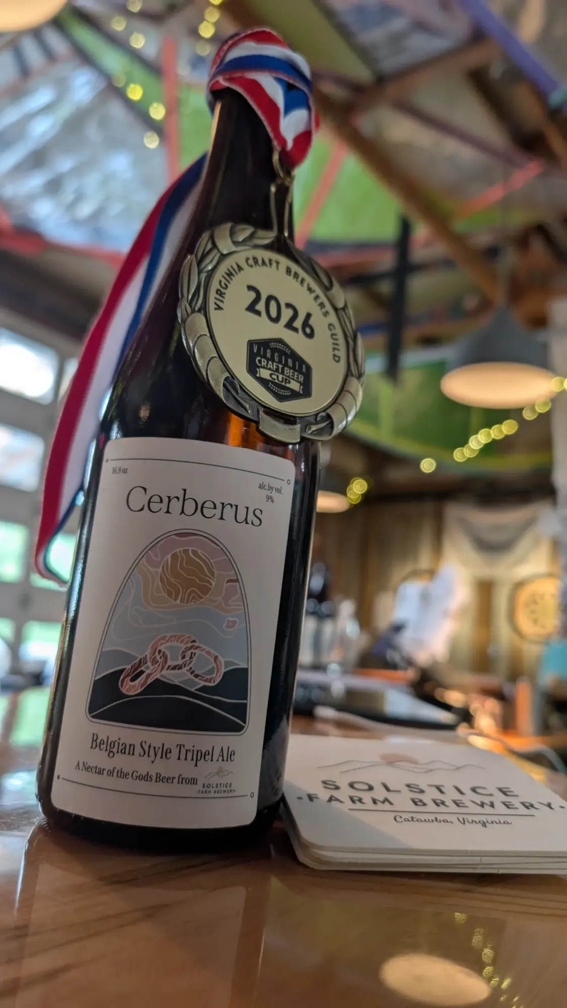 A bottle of Cerberus wine with a medal hanging from a ribbon, placed on a table in a decorated indoor setting.
