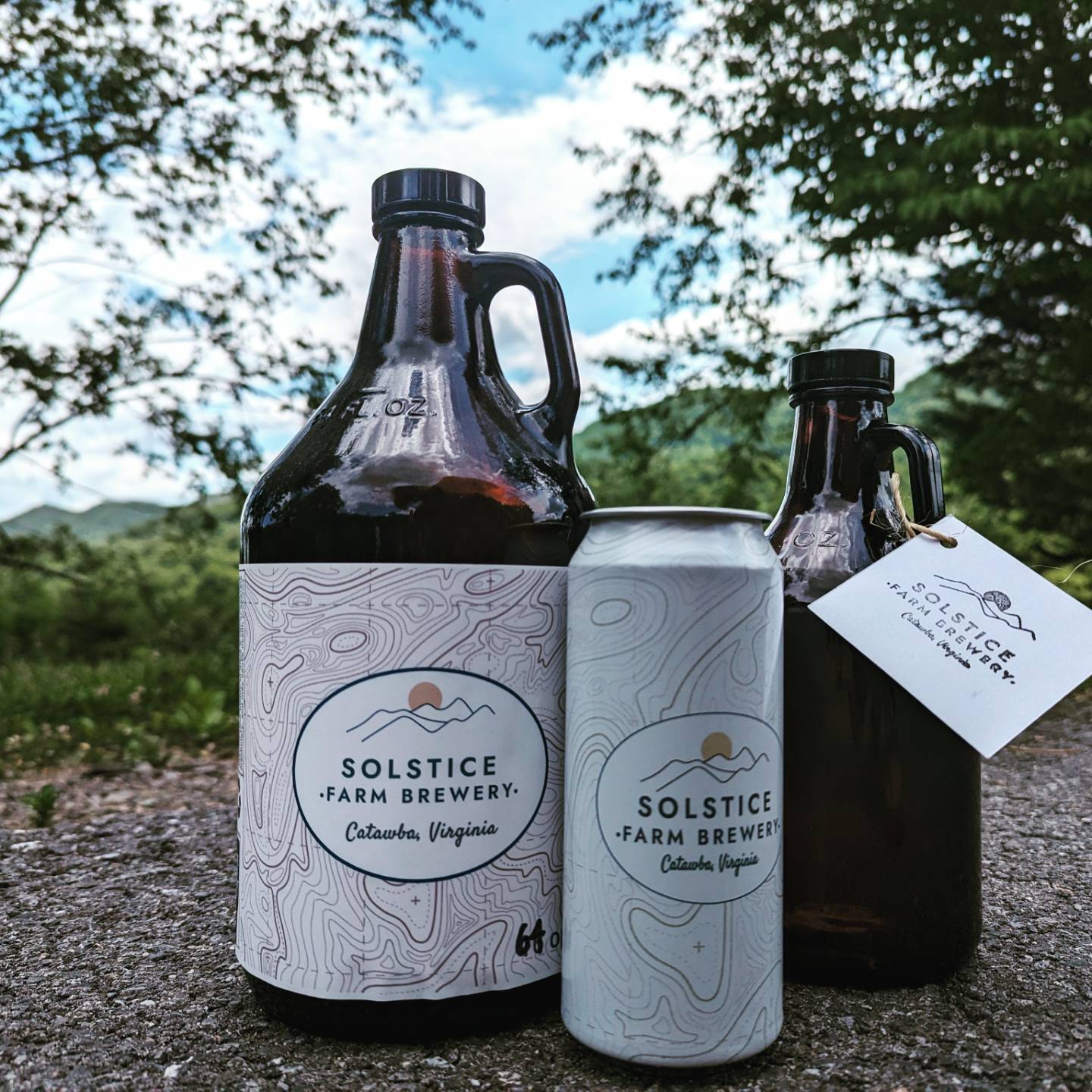Two bottles and a can of Solstice Farm Brewery beverages outdoors with trees and sky in background.