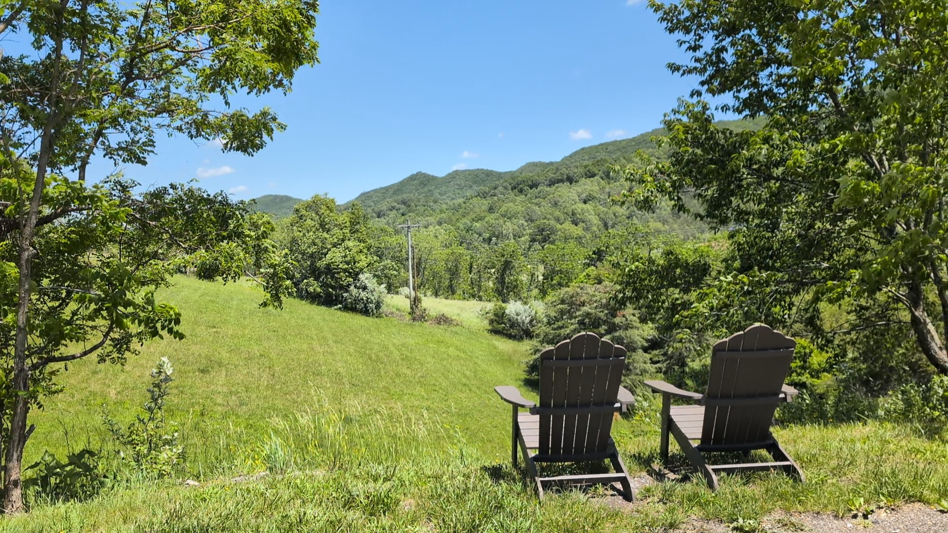 Two chairs face a scenic landscape with green hills and trees under a blue sky.