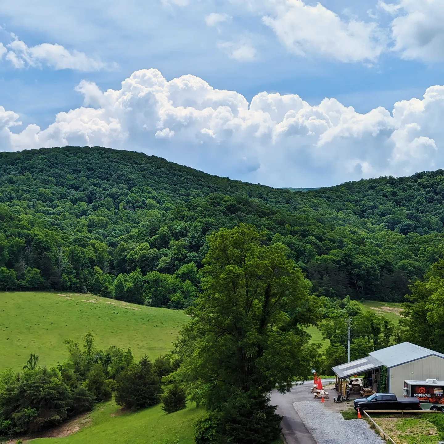 Scenic landscape with green hills, trees, a building, and a partly cloudy sky.