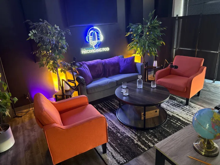 Indoor recording studio with purple and orange furniture, plants, and a neon sign reading 'Recording Food'.