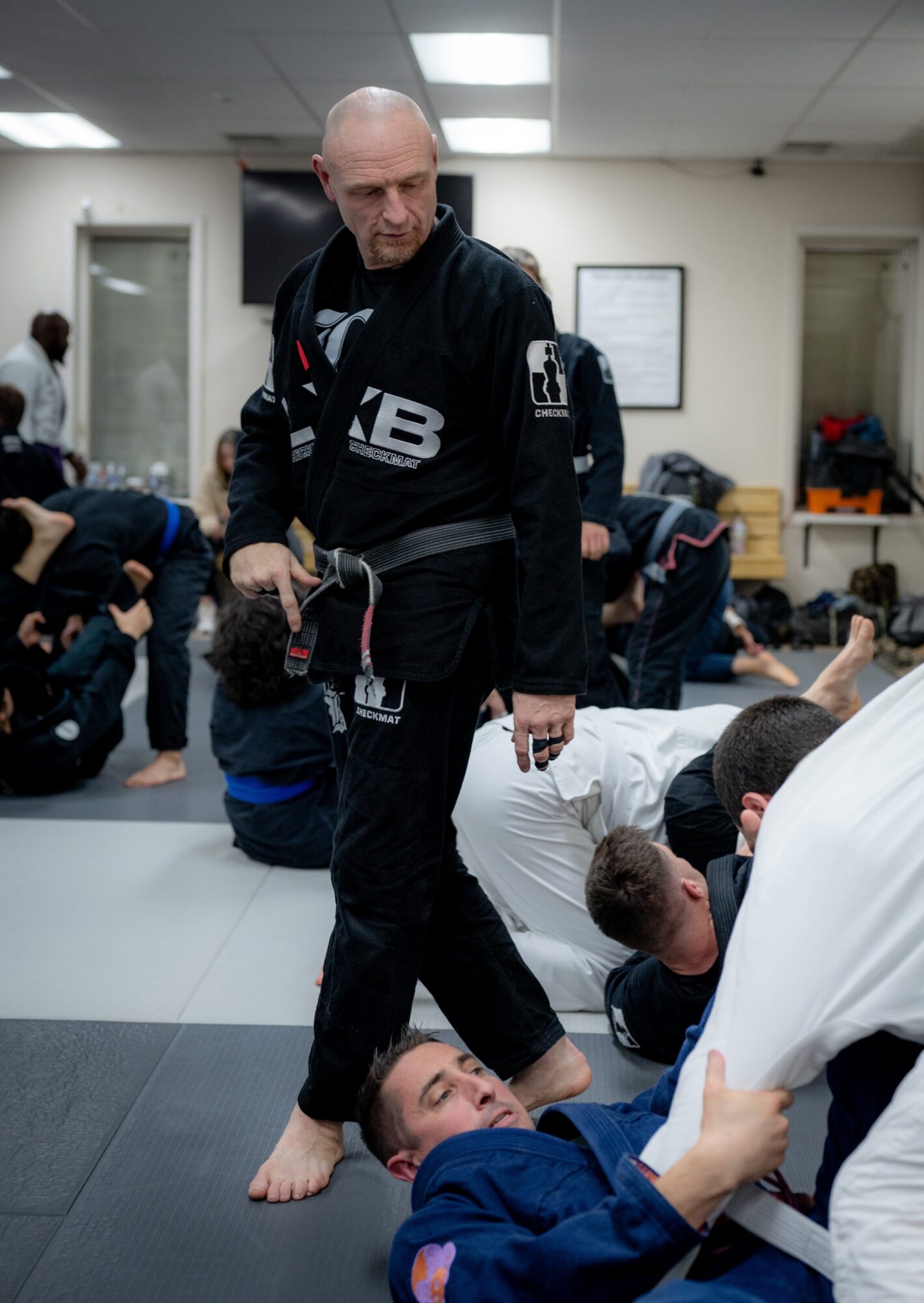 Martial arts class with instructor and students practicing on mats in a room with white walls and a TV screen.