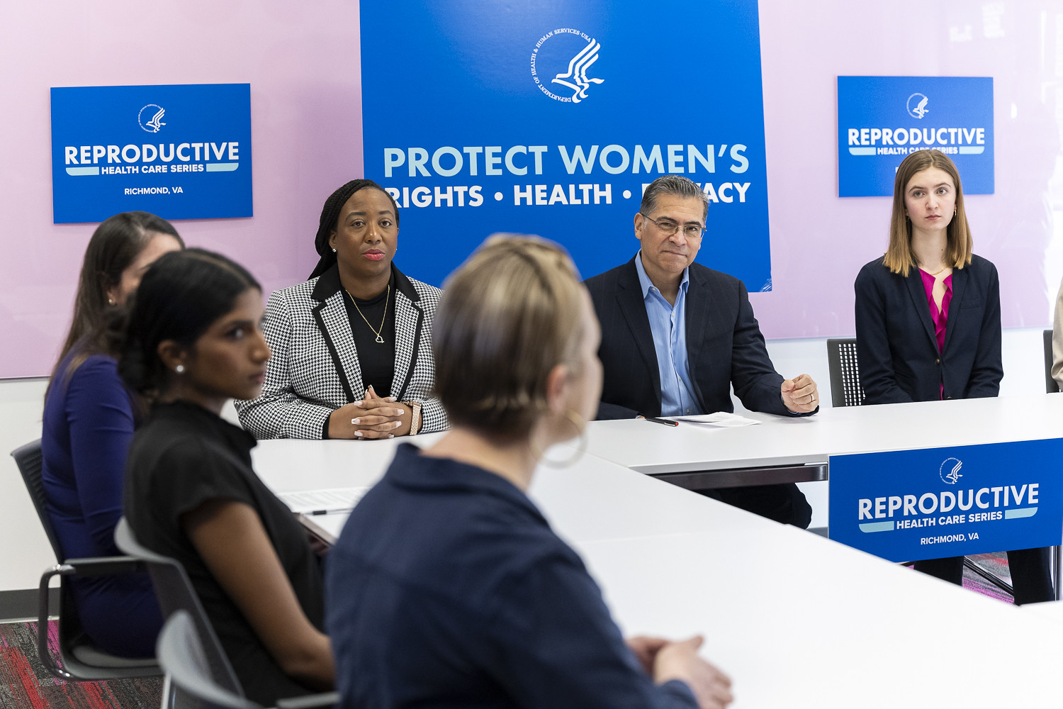 Group of five people seated at a panel discussion with signs about reproductive rights and health, in a conference room.